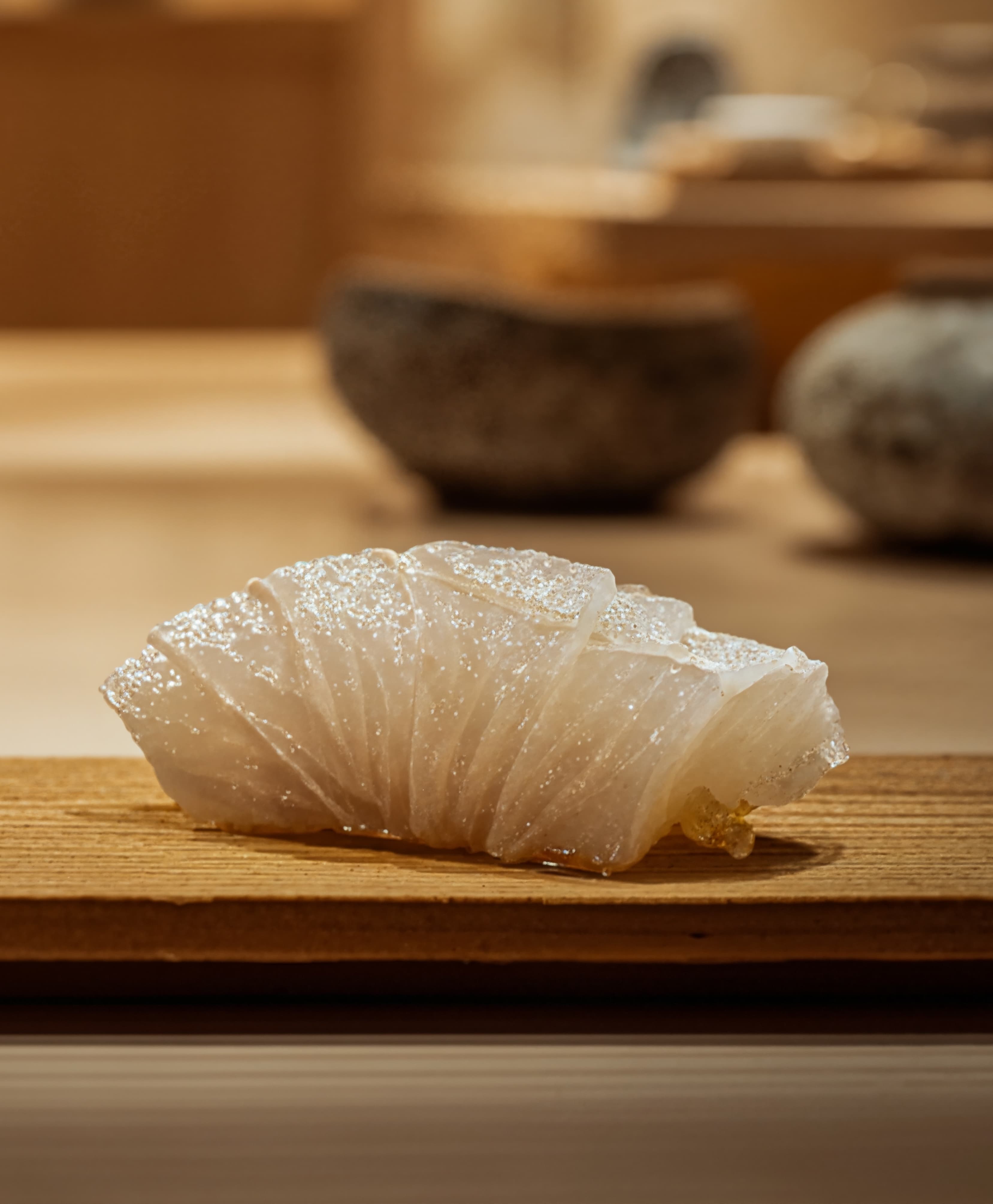 Close-up of translucent sushi slice with shiny texture on wooden board in warm light.