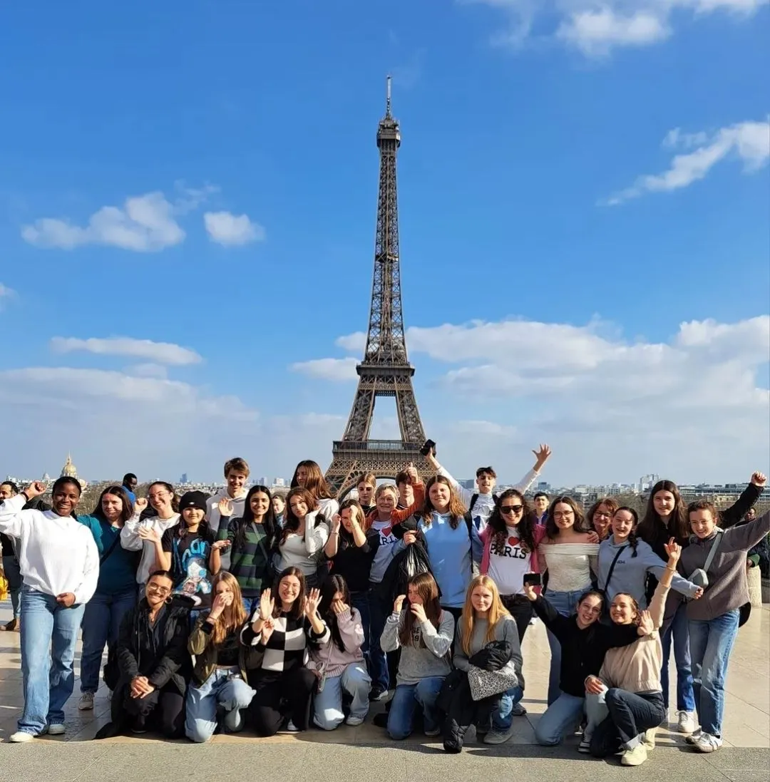 Group of young people posing happily in front of the Eiffel Tower in Paris on a sunny day.