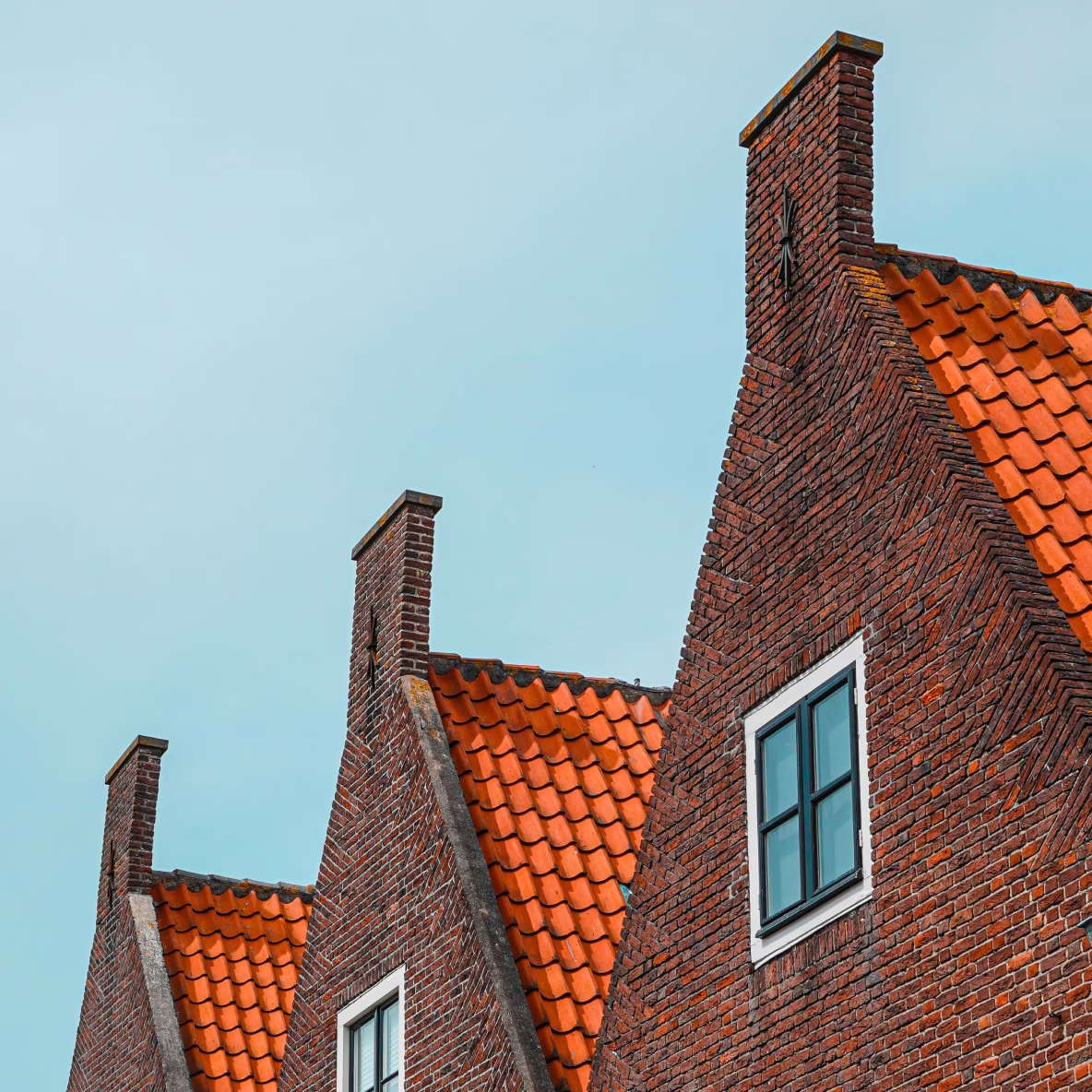 Drie rode bakstenen gevels met oranje dakpannen tegen een blauwe lucht.