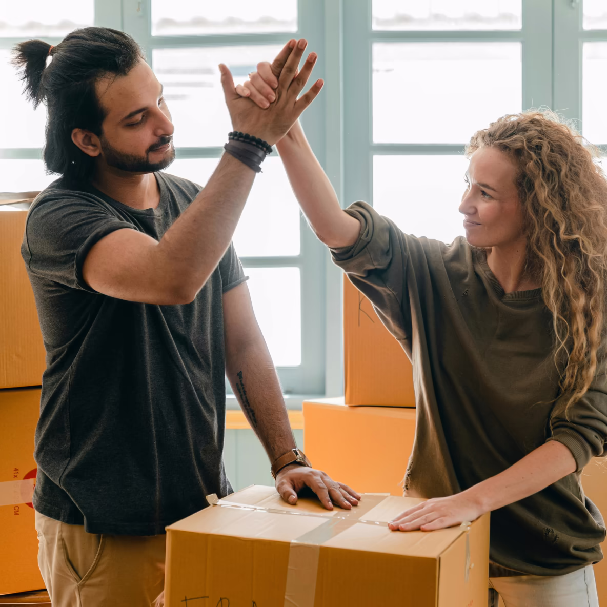 Twee volwassenen geven elkaar een high five terwijl ze dozen in een lichte kamer verplaatsen.