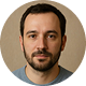 Portrait of a man with short dark hair, beard, and mustache against a plain beige background.
