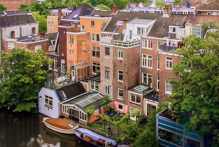 Canal-side view of residential buildings with boats docked and lush green trees in an urban setting.