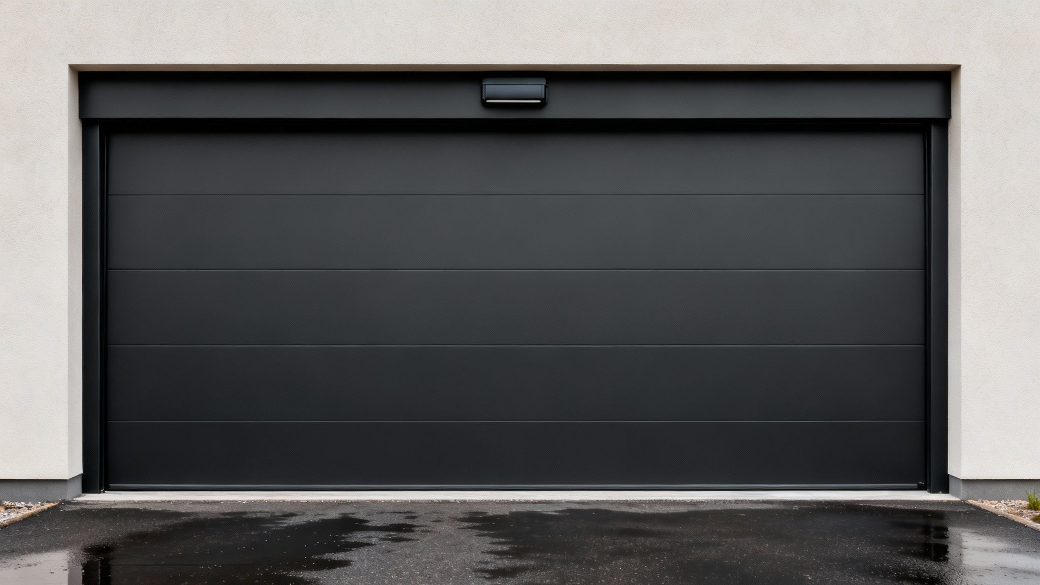 Porte de garage sectionnelle moderne en aluminium noir avec moteur, sur un mur clair, devant une allée mouillée.