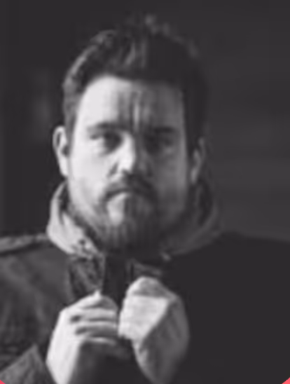 Blurred black and white portrait of a man with beard adjusting his jacket collar.