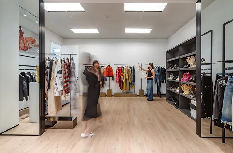 Chelsey House showroom interior with wooden floor, racks of colorful clothes, shelves of shoes, and two people browsing.