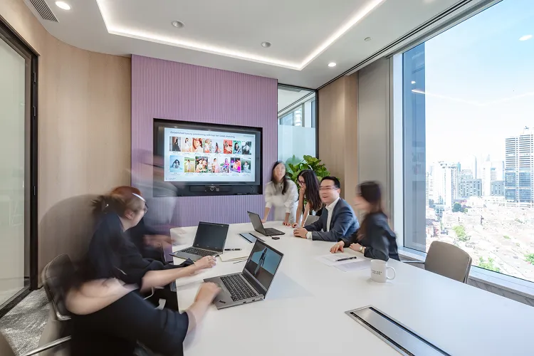 Blurry image of Chelsey house meeting room with six people having a meeting around a white table with laptops.