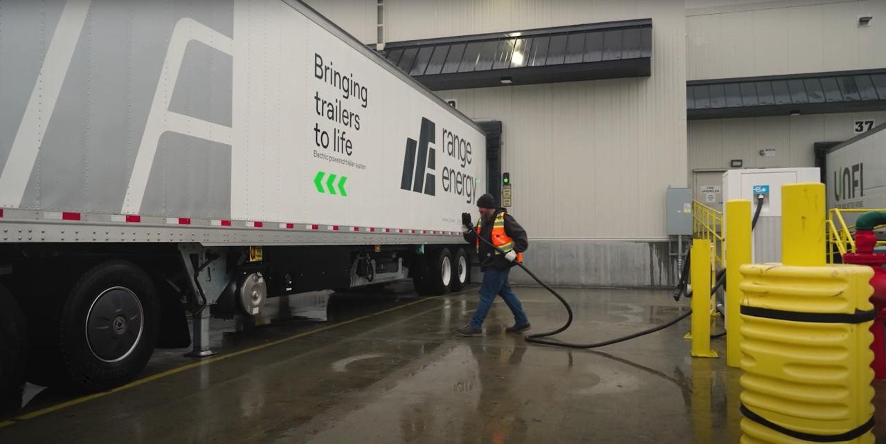 Warehouse worker plugging a charging cable into a Range eTrailer at a distribution center dock