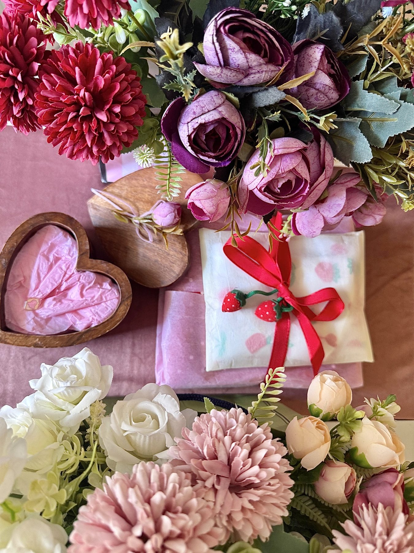 Wooden heart keepsake box and ribbon-tied wrapped gift surrounded by faux florals