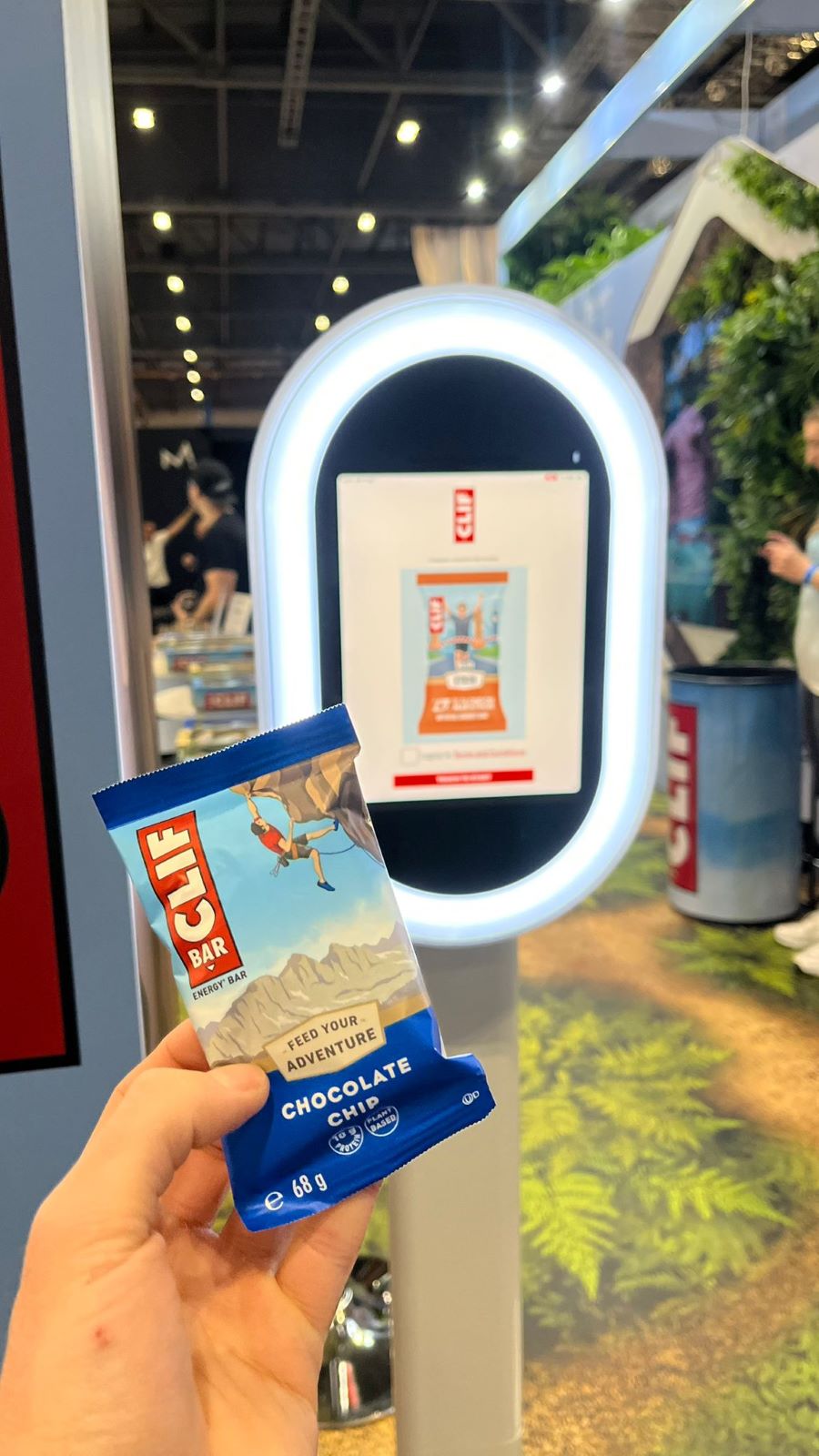 A CLIF Bar held up in front of the booth screen displaying a finished AI Official Energy Bar pack.