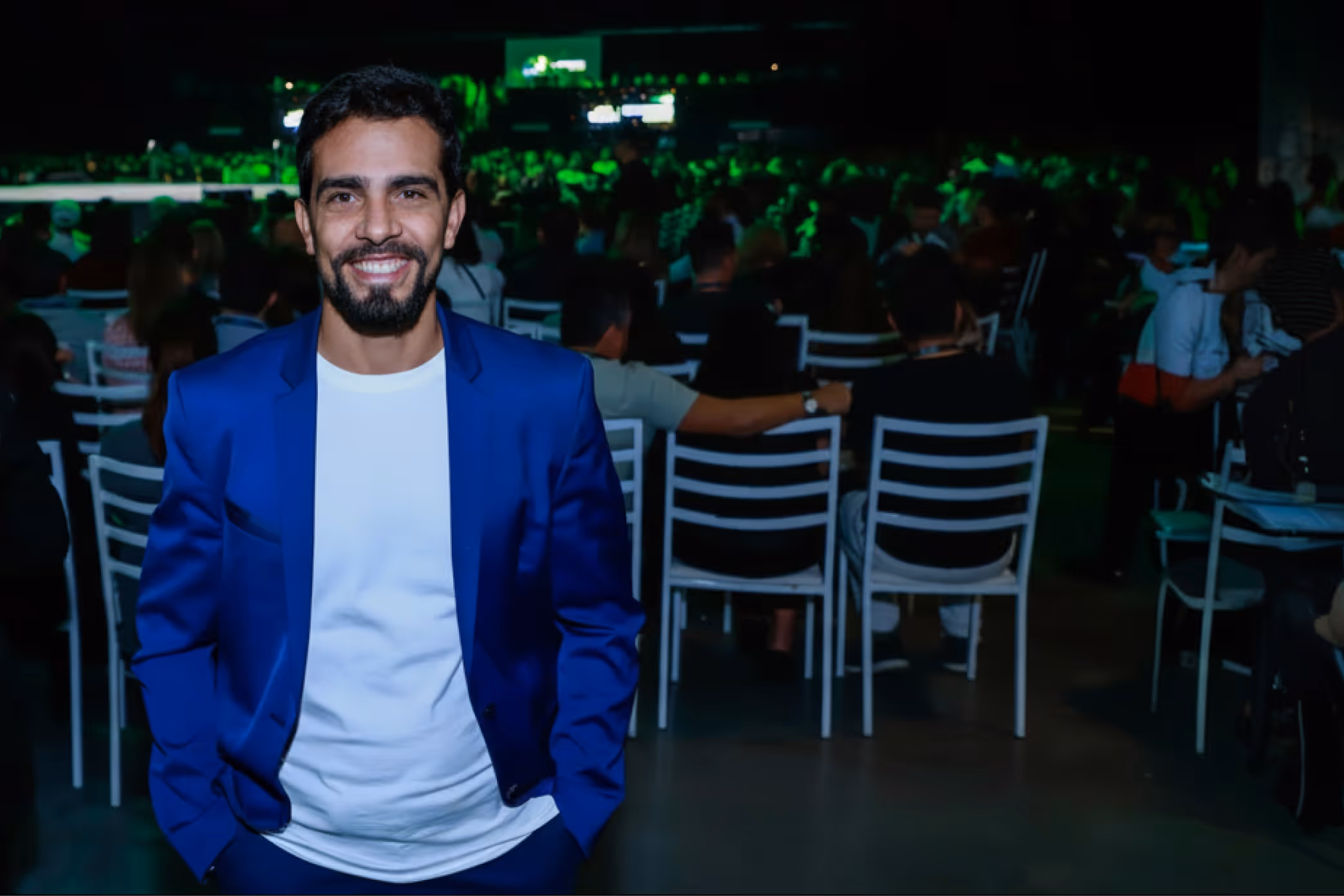 Diogo Póvoa vestindo terno azul e camiseta branca em evento.
