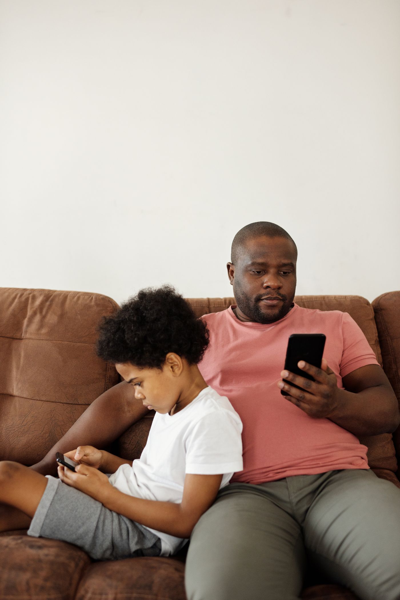 A father and son sitting on a sofa, each using a phone