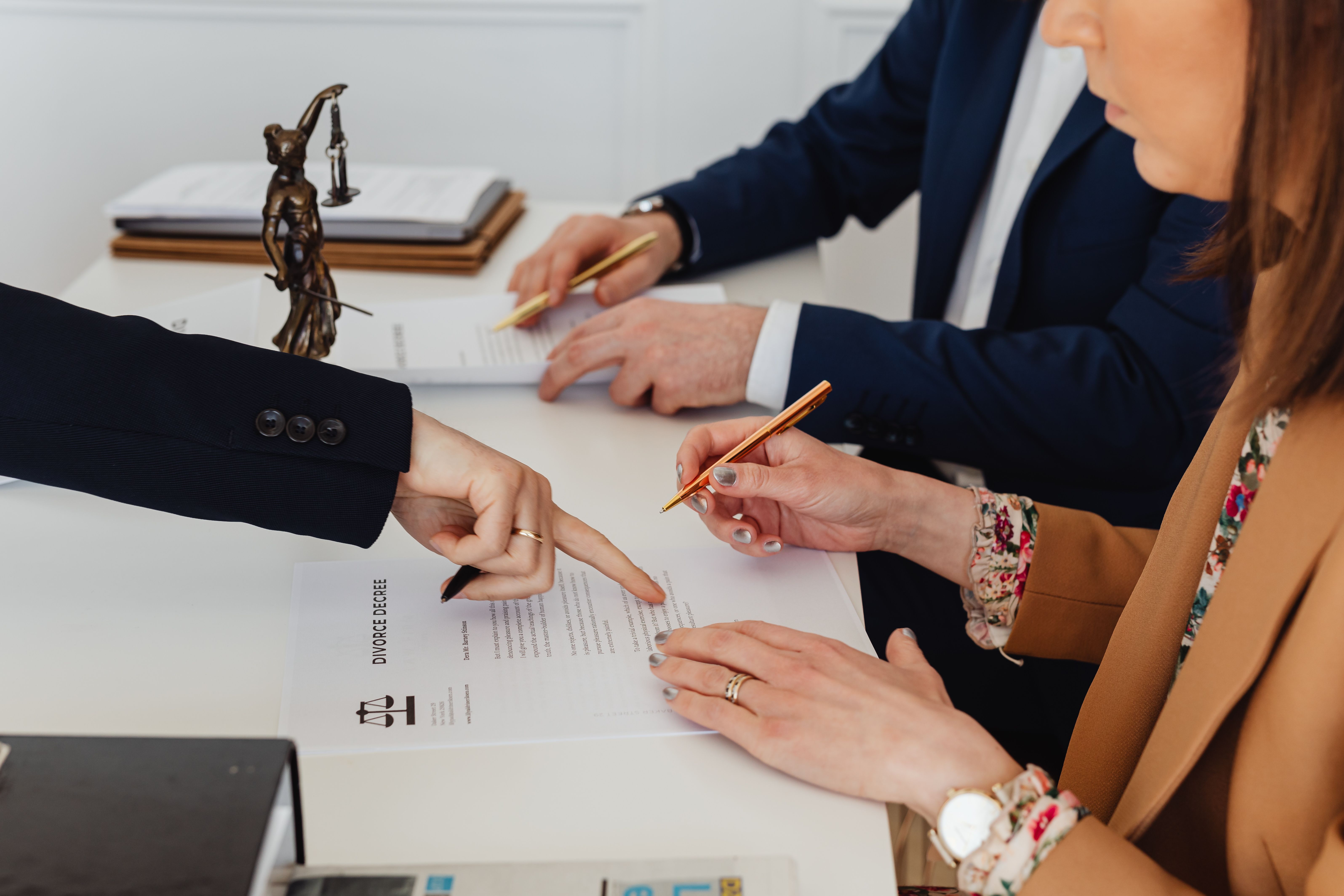 A lawyer and client reviewing and signing divorce documents at a desk, with a Lady Justice statue in the background.