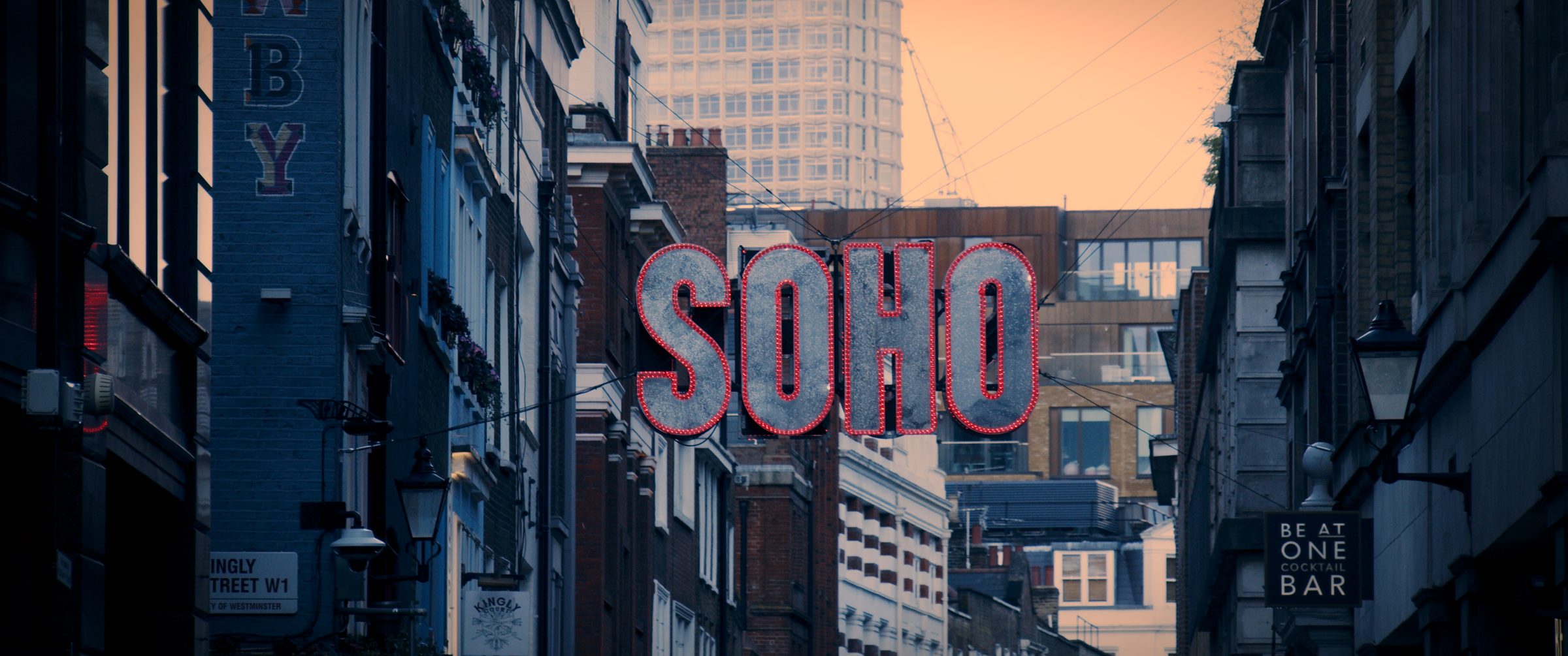 A Soho street in London at dusk beneath a neon sign