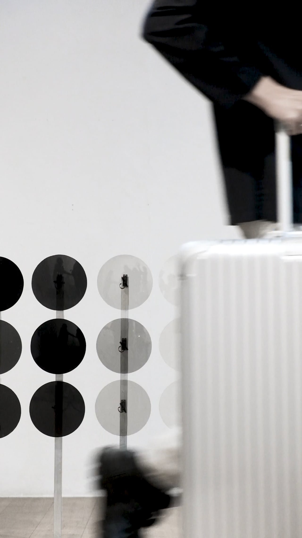 The Dots installation beside a white RIMOWA suitcase seen through rows of polarised discs