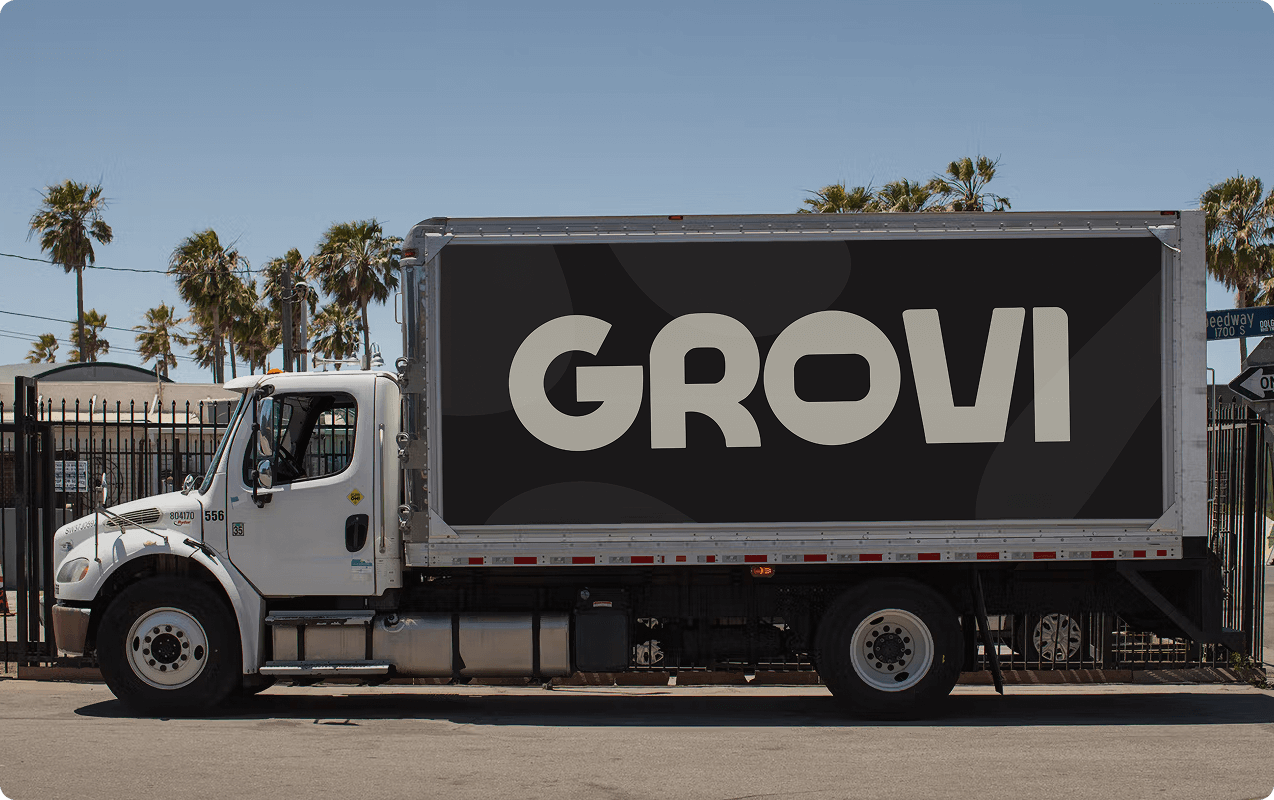 Side view of a white delivery truck with a large black sign on the cargo area displaying the word 'GROVI'.