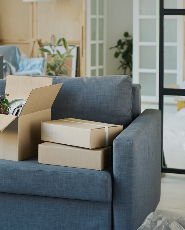 Cardboard moving boxes placed on a blue sofa in a living room during a move.