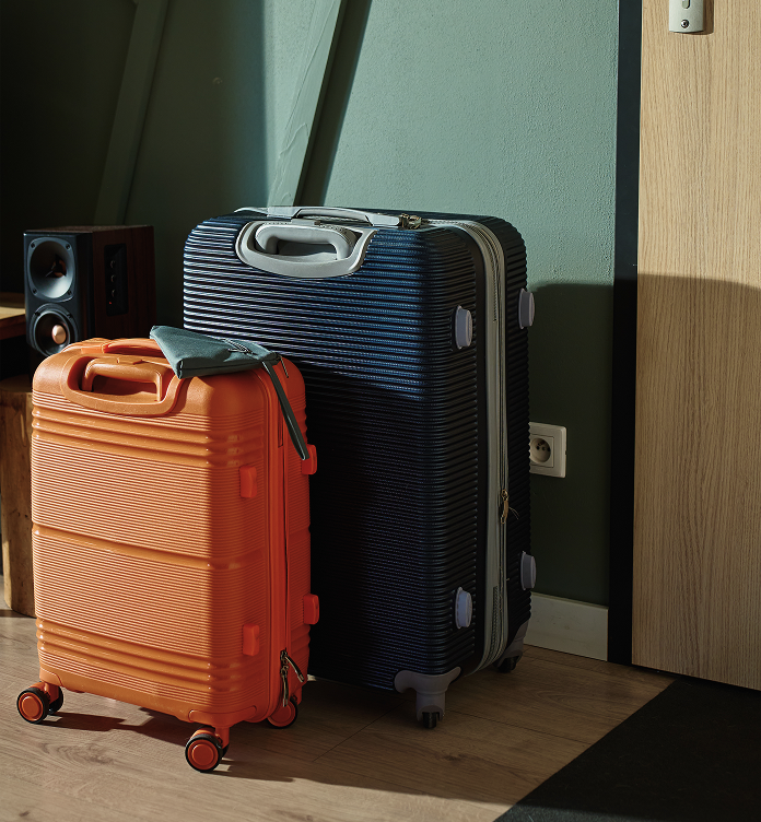 Two hard-shell suitcases, one orange and one navy blue, standing on a wooden floor near a green wall and a wooden door.