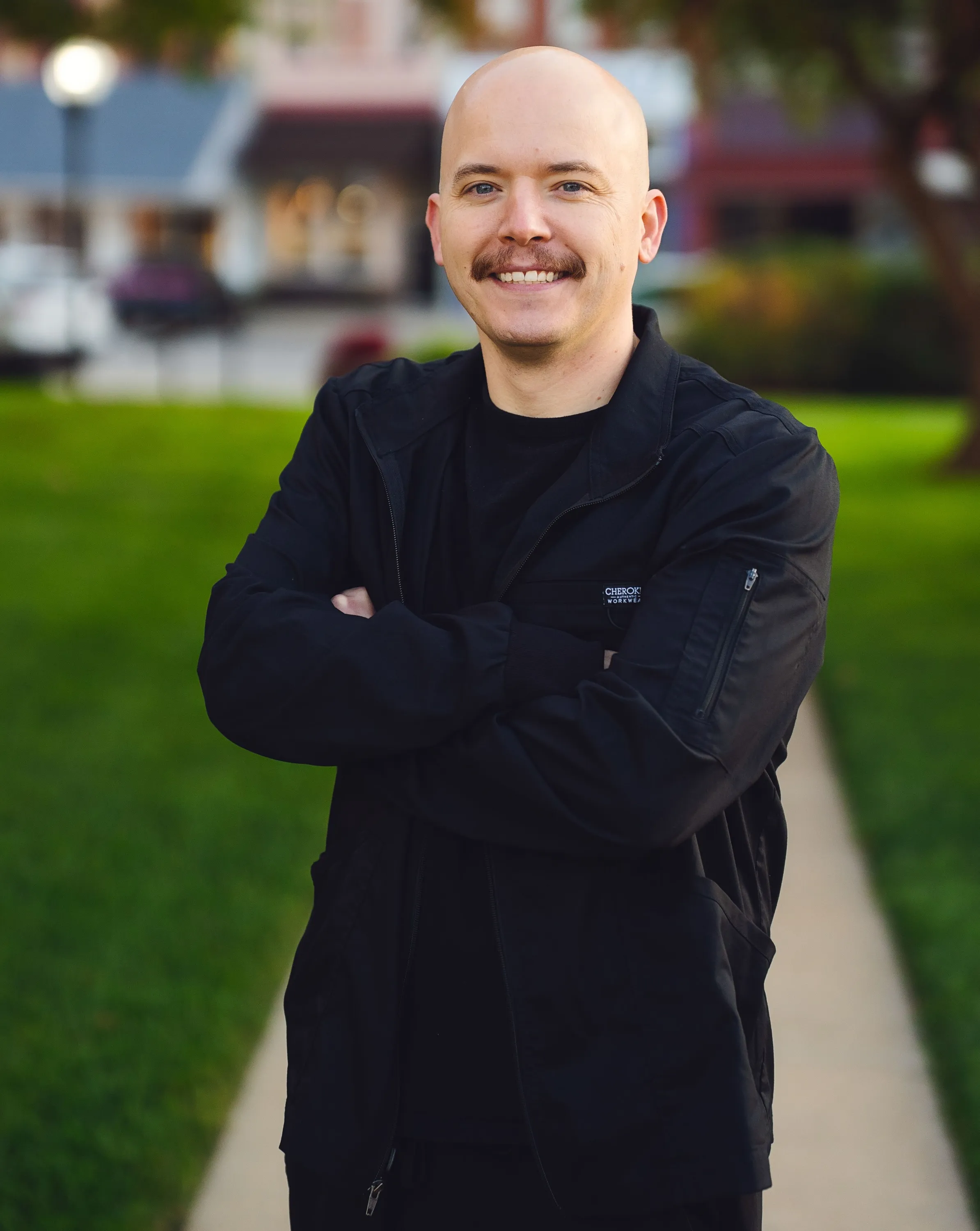 Portrait of Dr. Roy Burkhalter standing outdoors on a tree-lined sidewalk in Harlan
