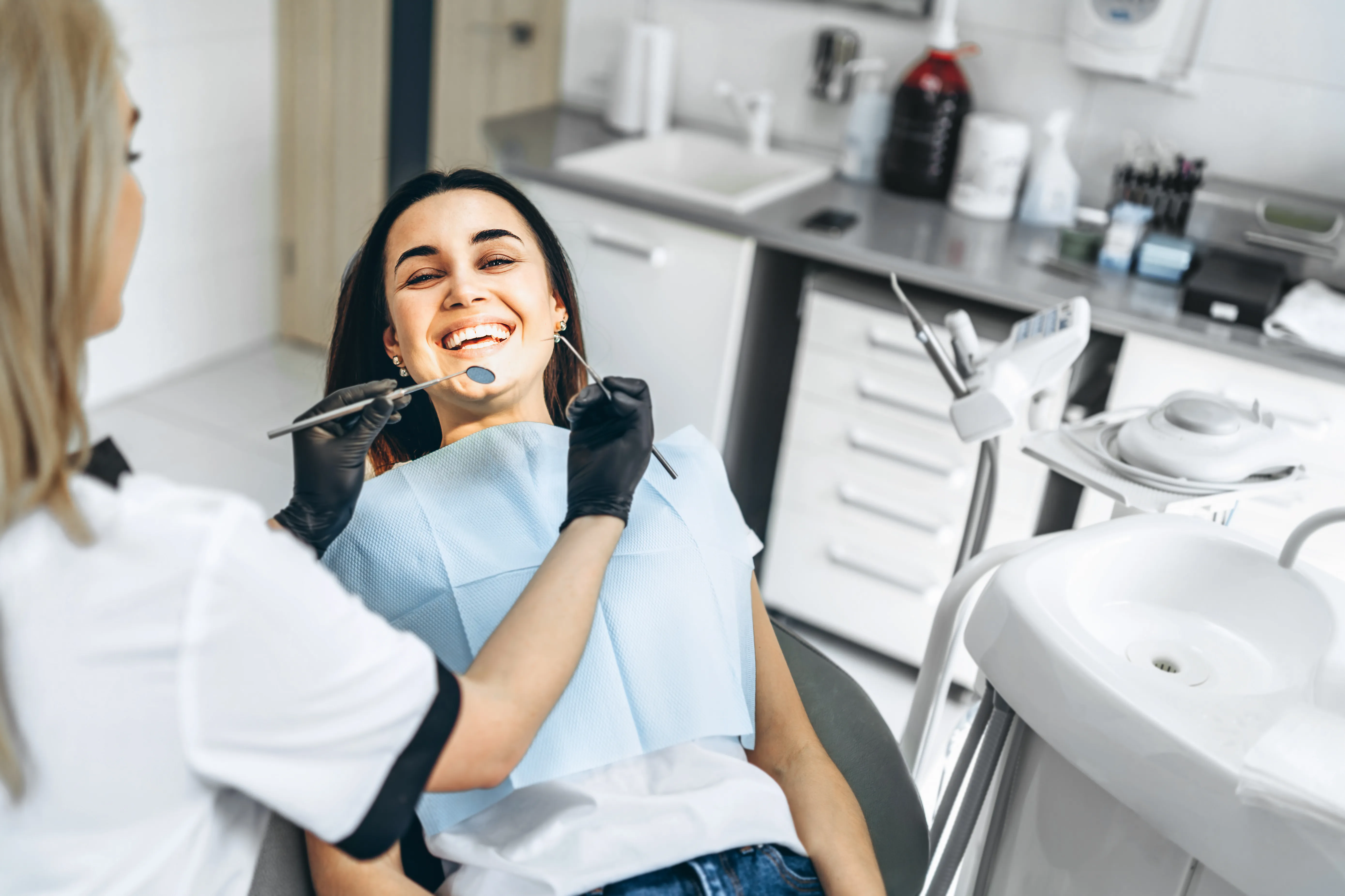 `Young woman smiling in a dental chair while a hygienist works at her mouth during a cosmetic visit