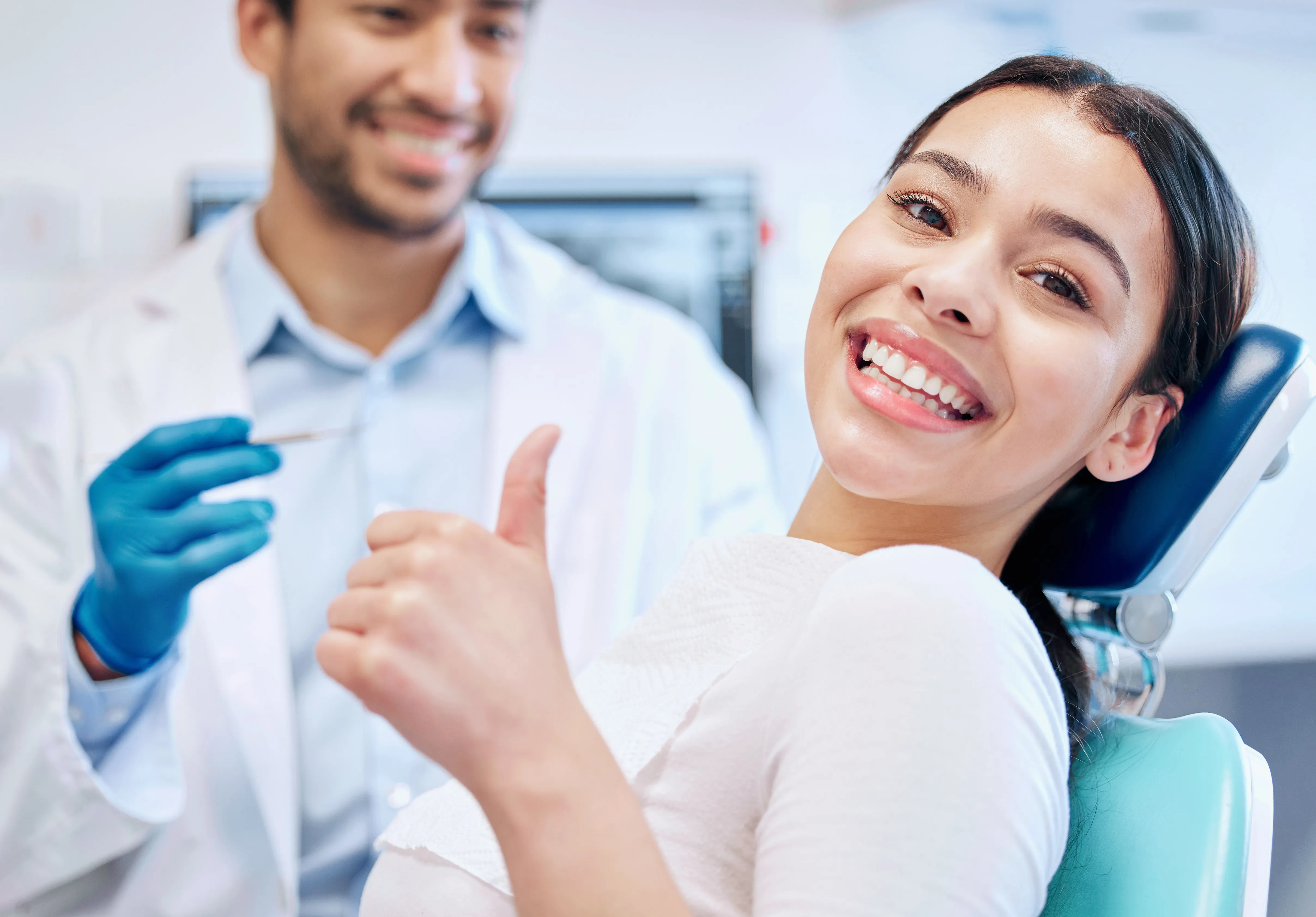 Smiling woman giving a thumbs-up in a dental chair next to a male dentist