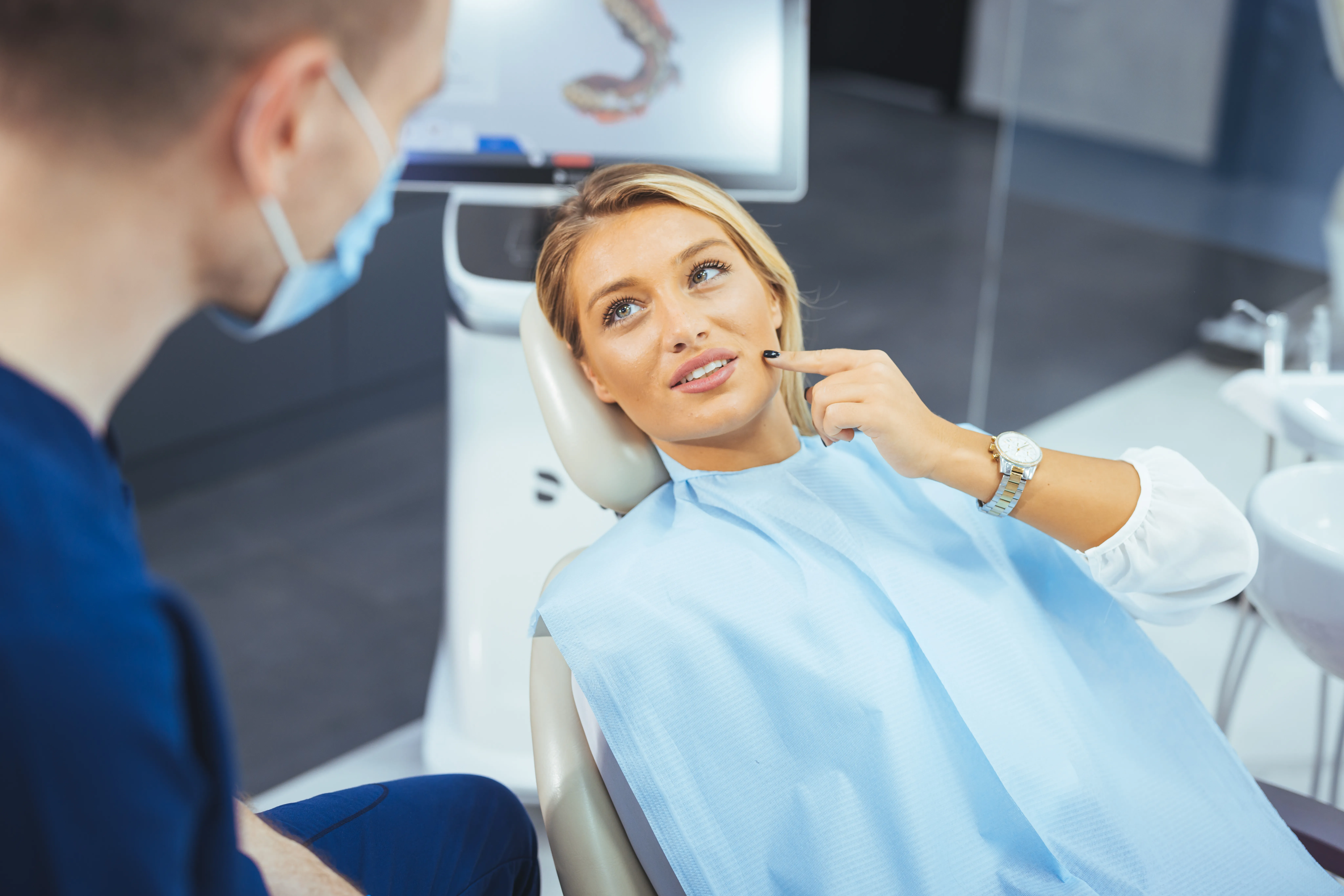 Patient smiling in the dental chair during an implant consultation, with a 3D scan on the monitor