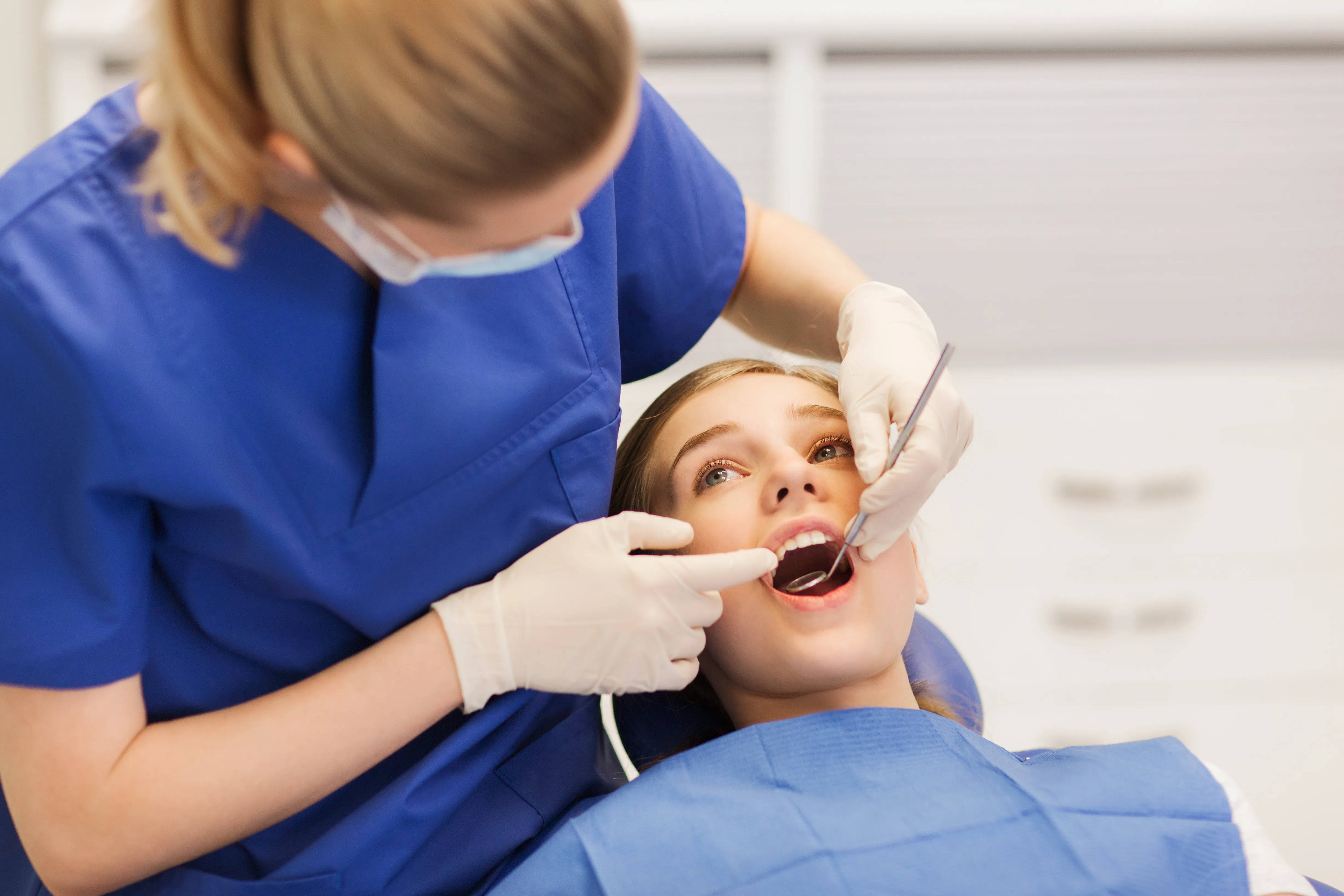 Dentist examining a reclined patient's teeth with a mirror and explorer