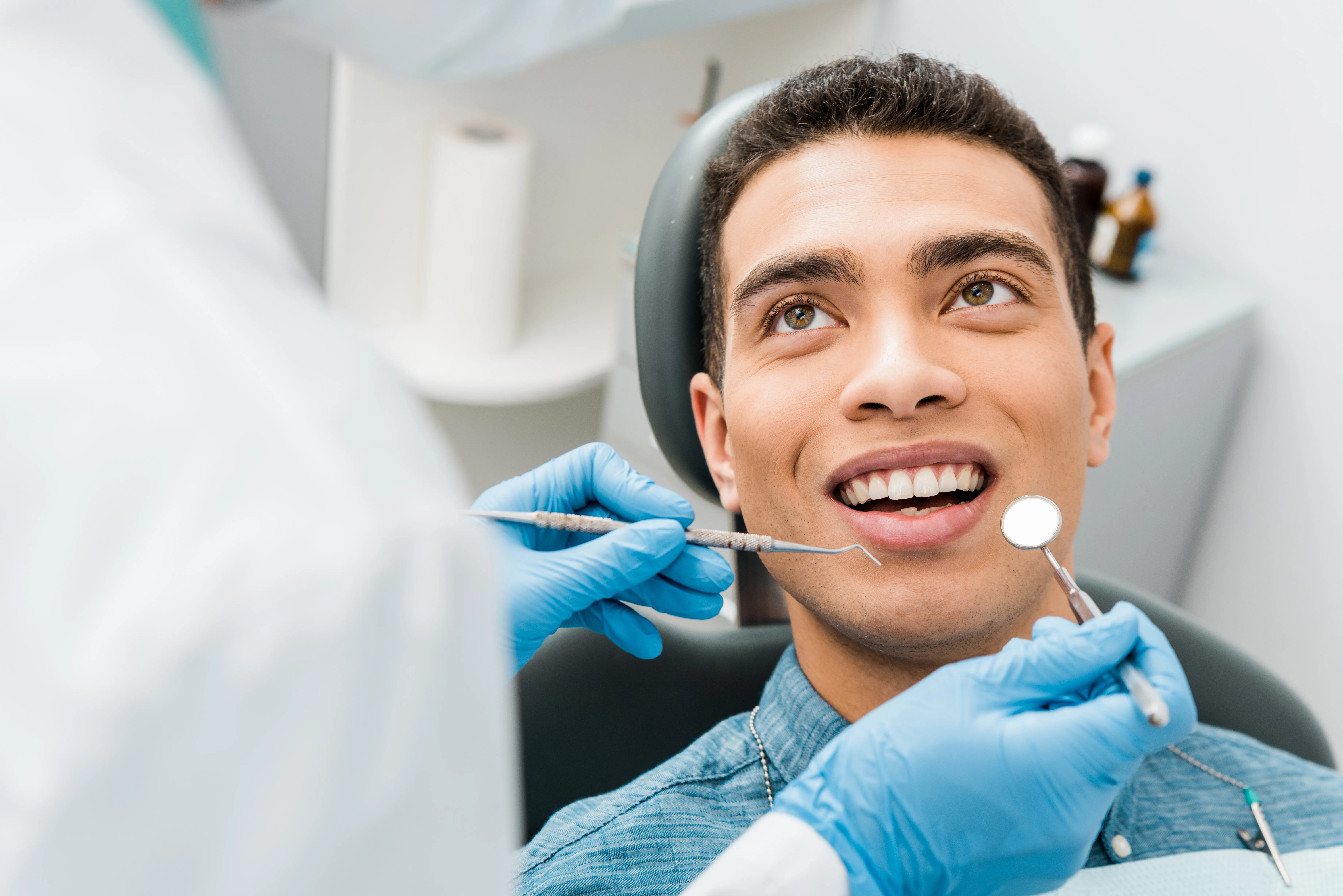 Smiling young man in the dental chair during a checkup with a mirror and explorer