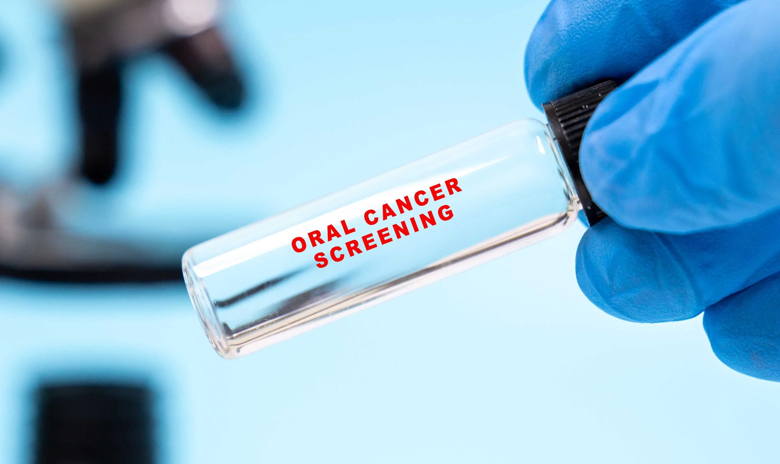 Gloved hand holding a laboratory vial labeled Oral Cancer Screening