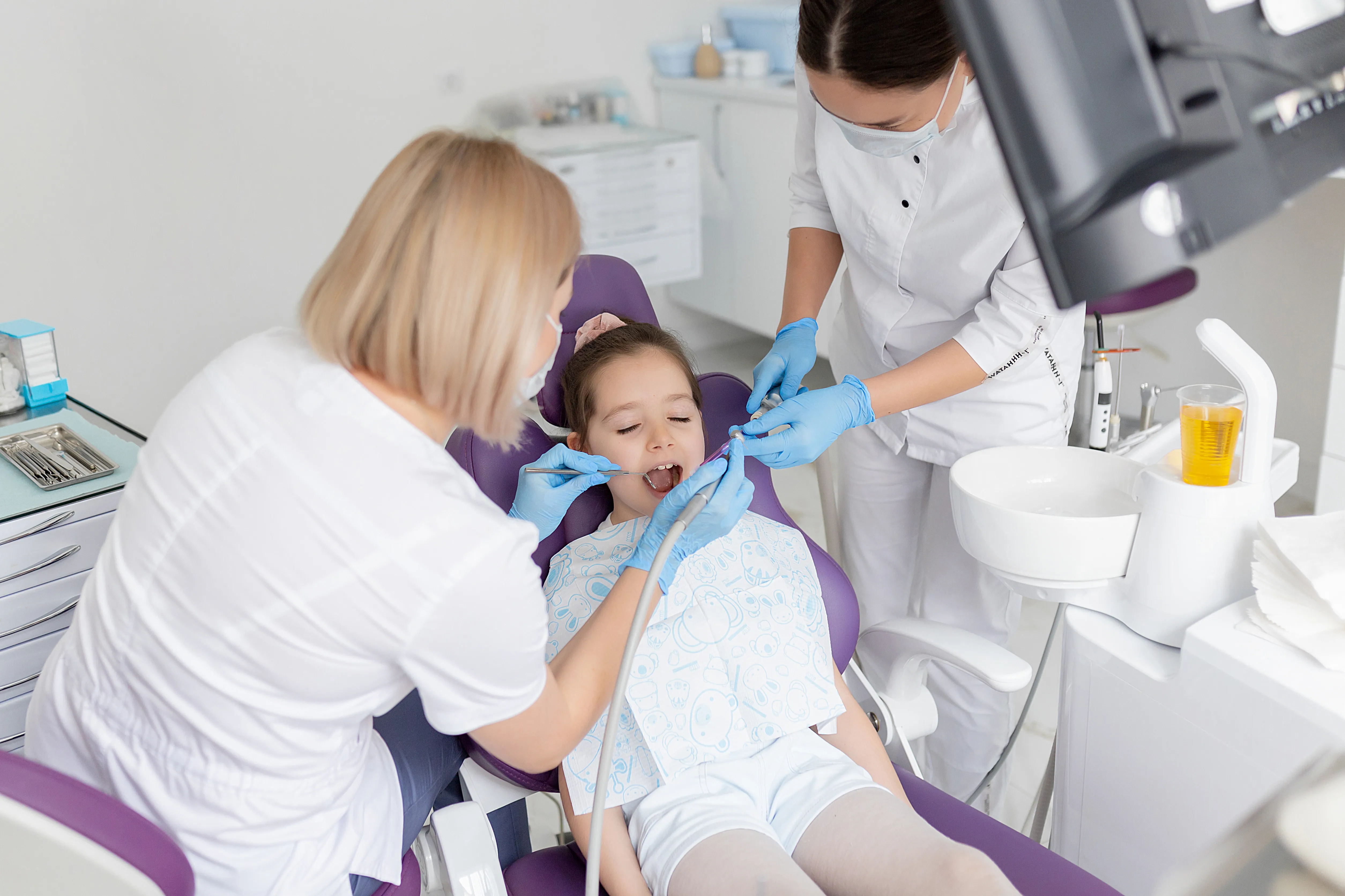 Child receiving dental treatment from a dentist and assistant in a treatment room