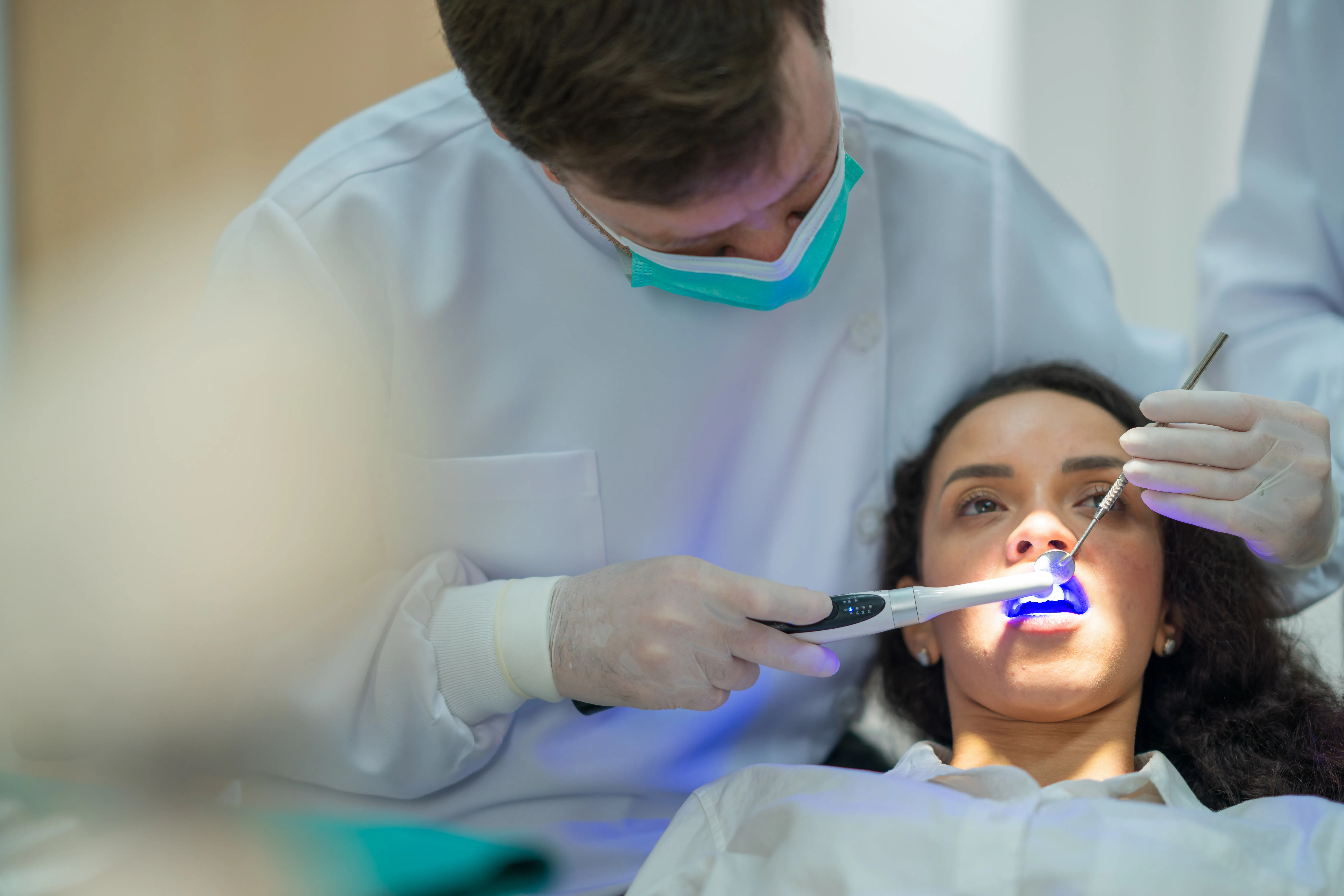 Dentist using a blue curing light on a woman's teeth during a dental visit
