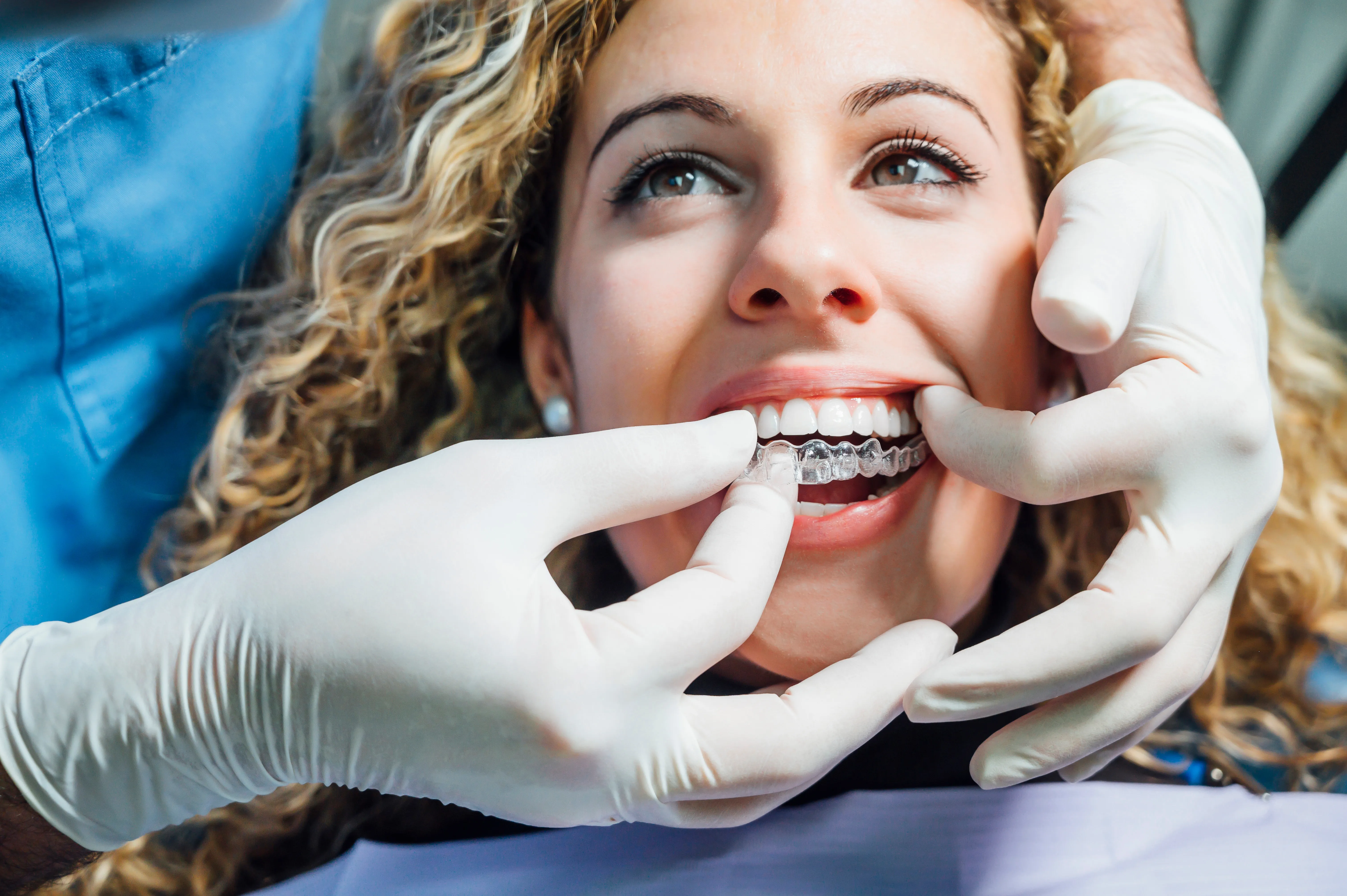 Gloved orthodontist fitting a clear ceramic bracket onto a young woman's tooth