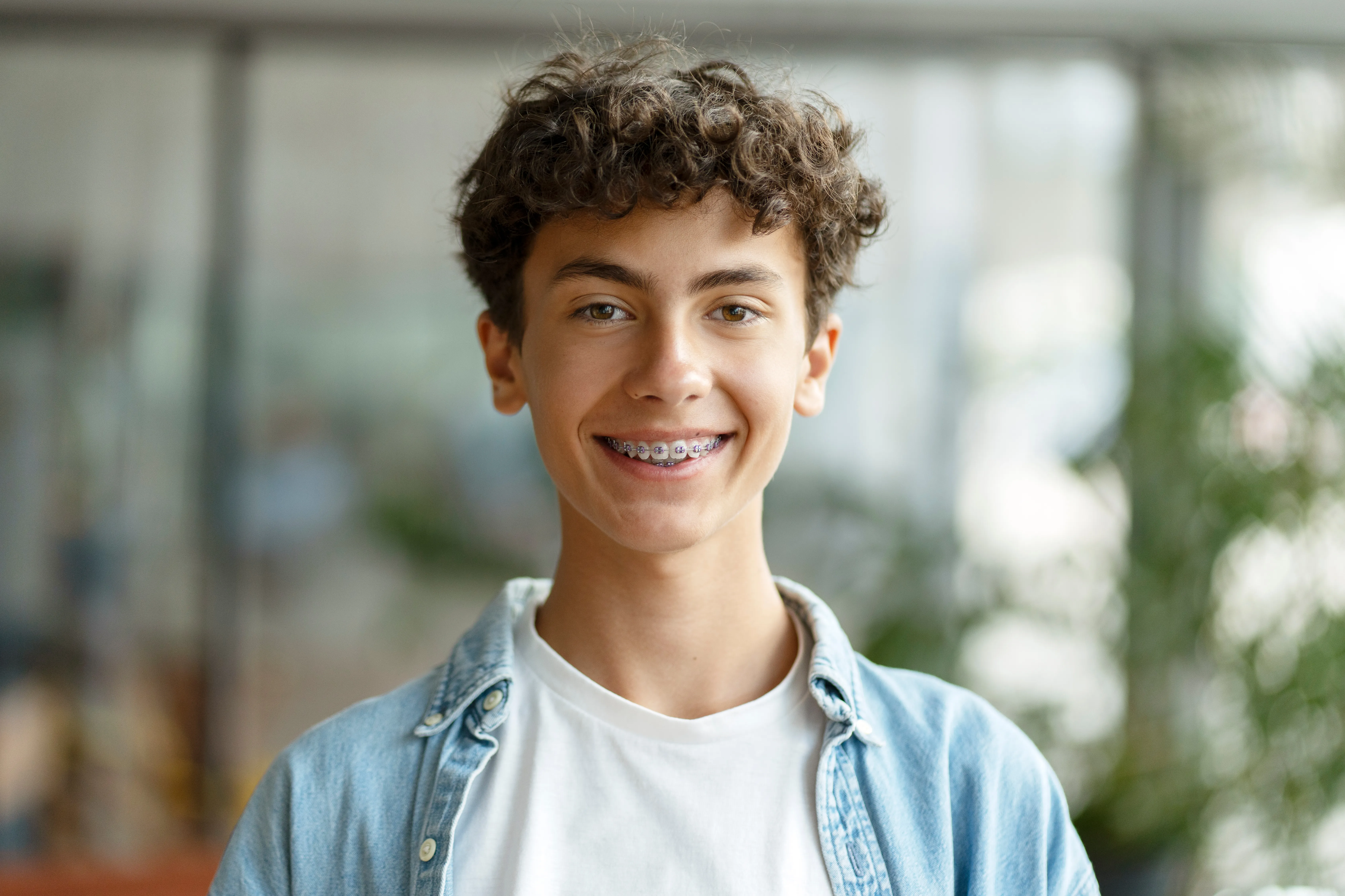 Smiling teenage boy with metal braces wearing a denim shirt indoors