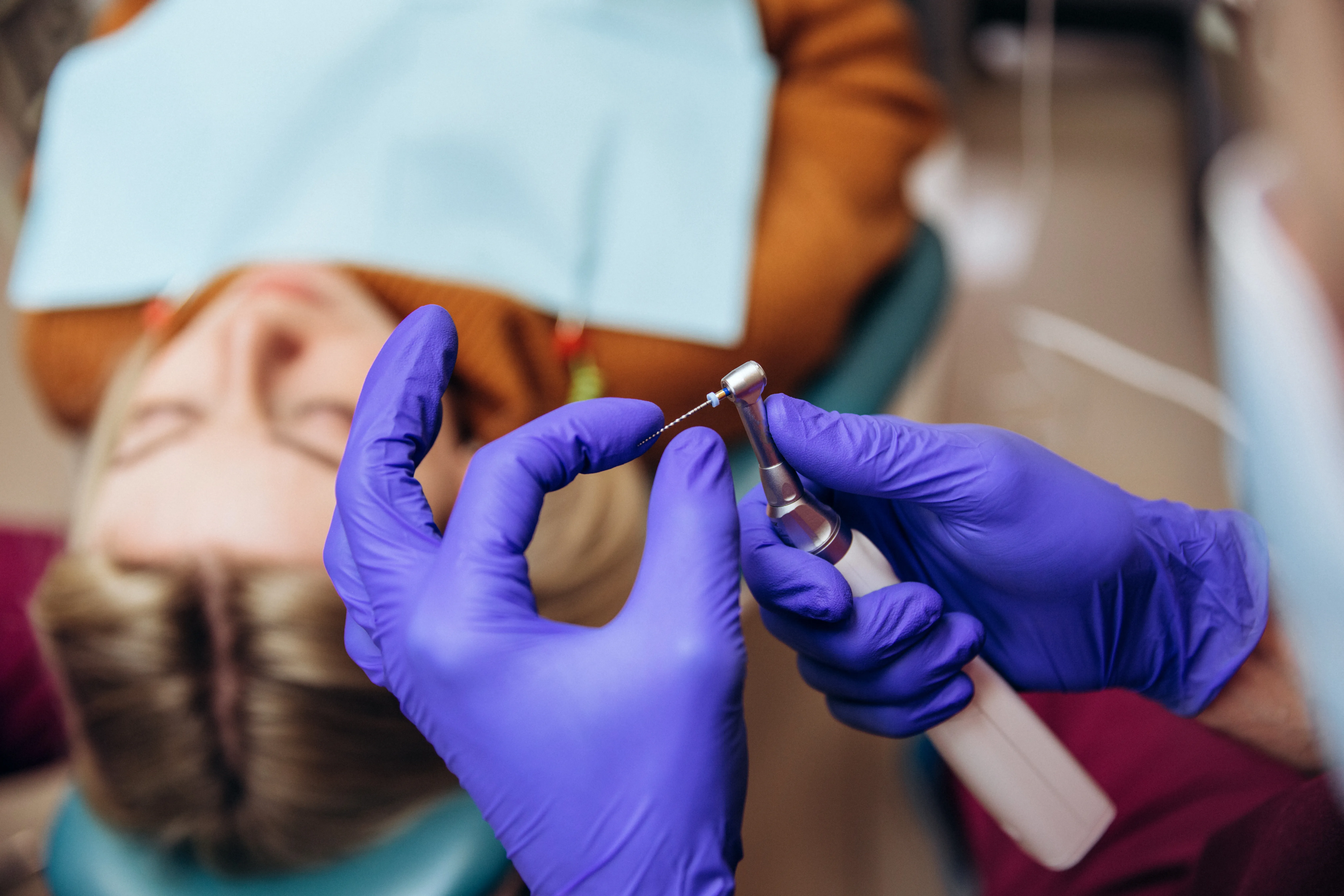Dentist in purple gloves preparing a local anesthetic syringe beside a reclined patient