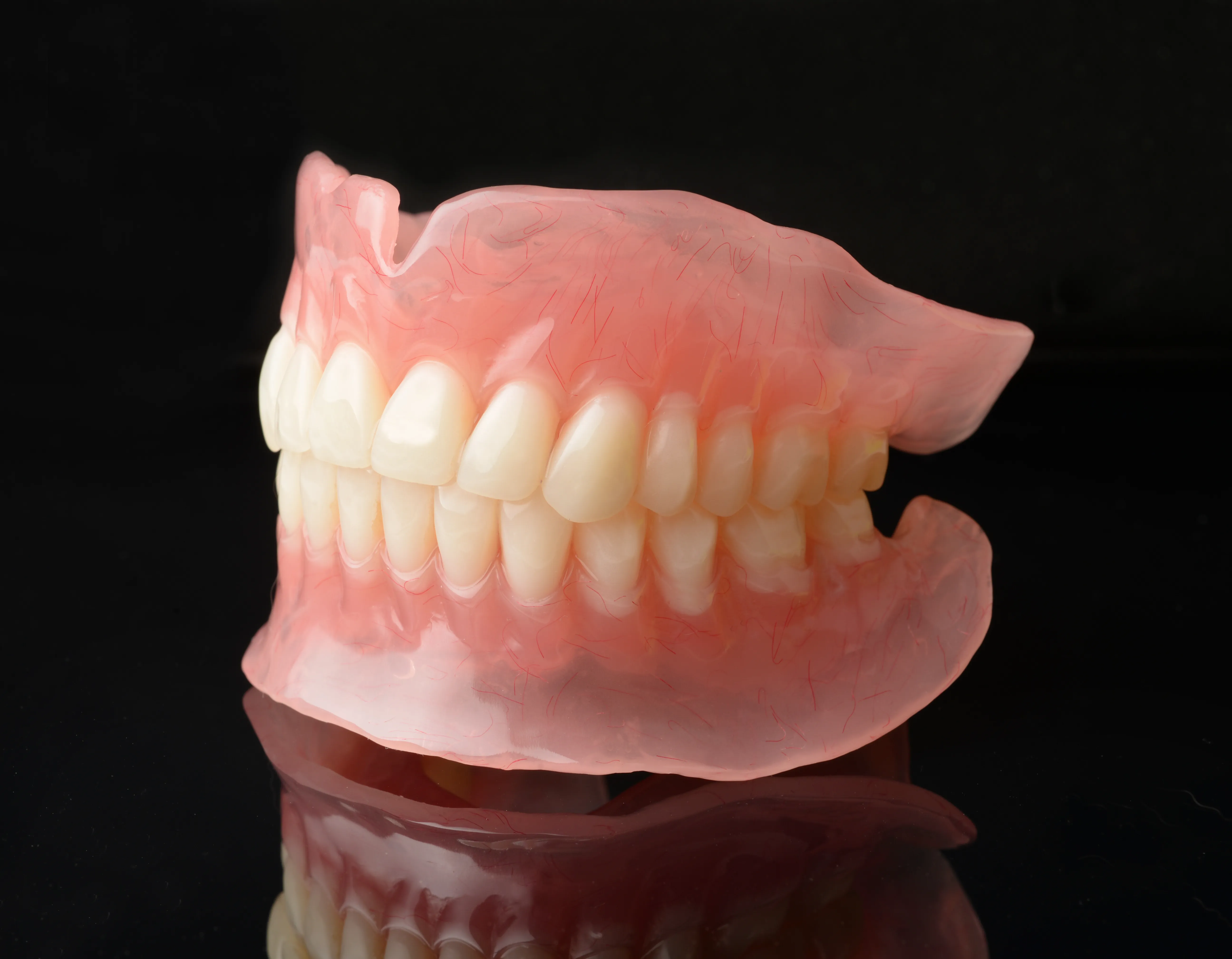 A full set of removable upper and lower acrylic dentures on a dark background