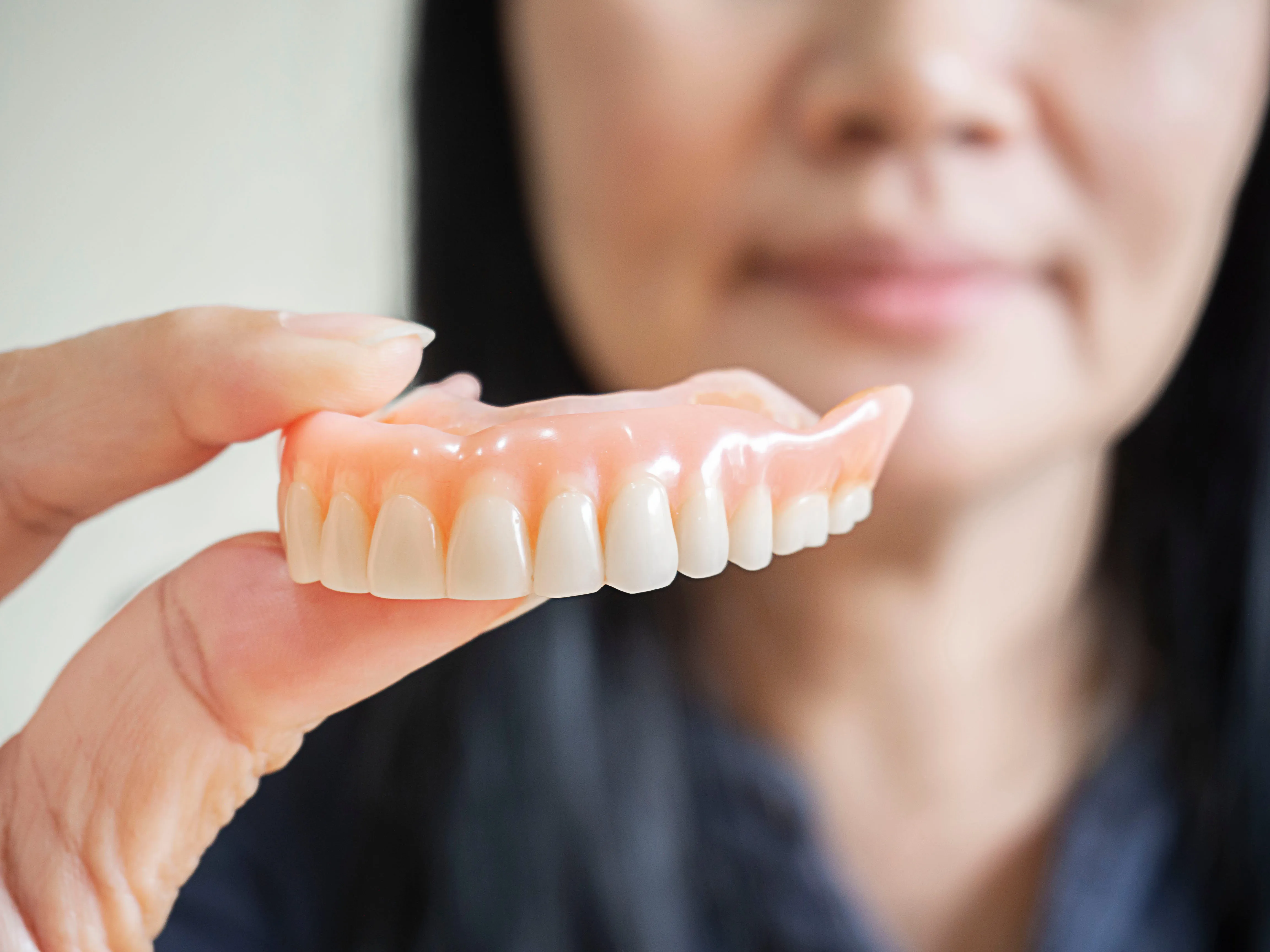 Older woman holding a full upper acrylic denture up in front of her mouth