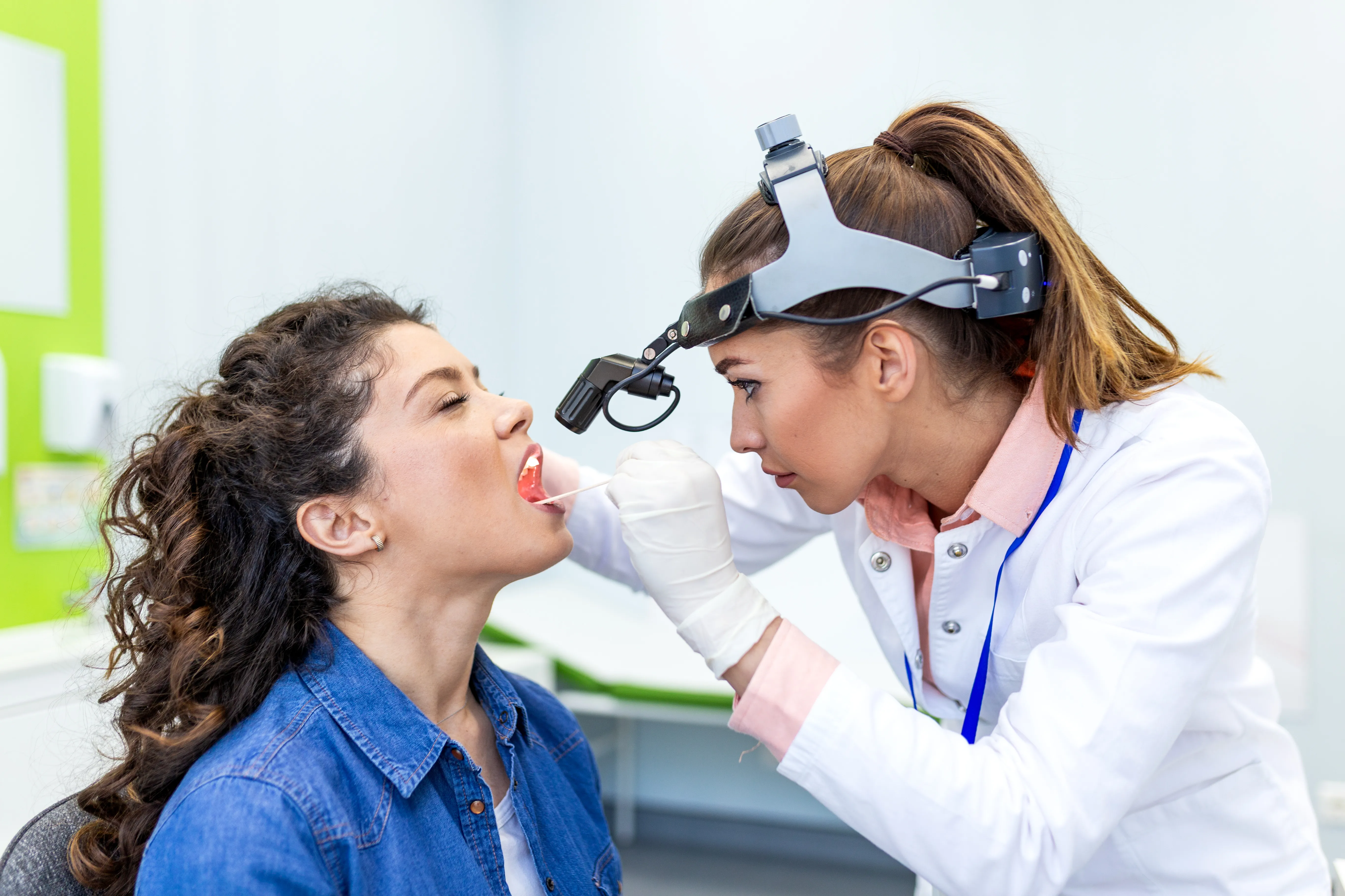 Clinician using a headlight to examine a patient's mouth and throat during a screening
