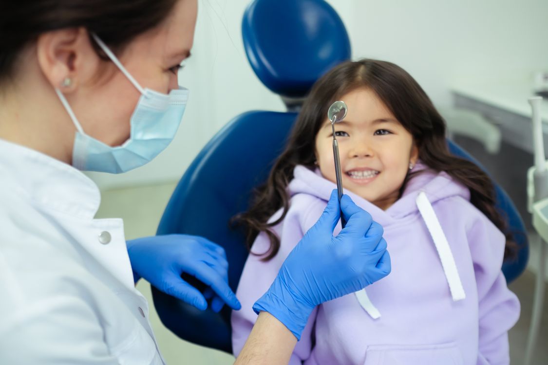 Dentist showing a dental mirror to a smiling child during a pediatric checkup