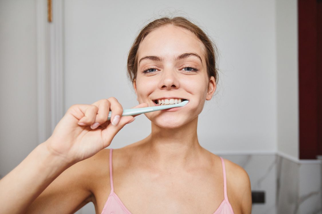Woman smiling while brushing her teeth as part of a daily oral-care routine