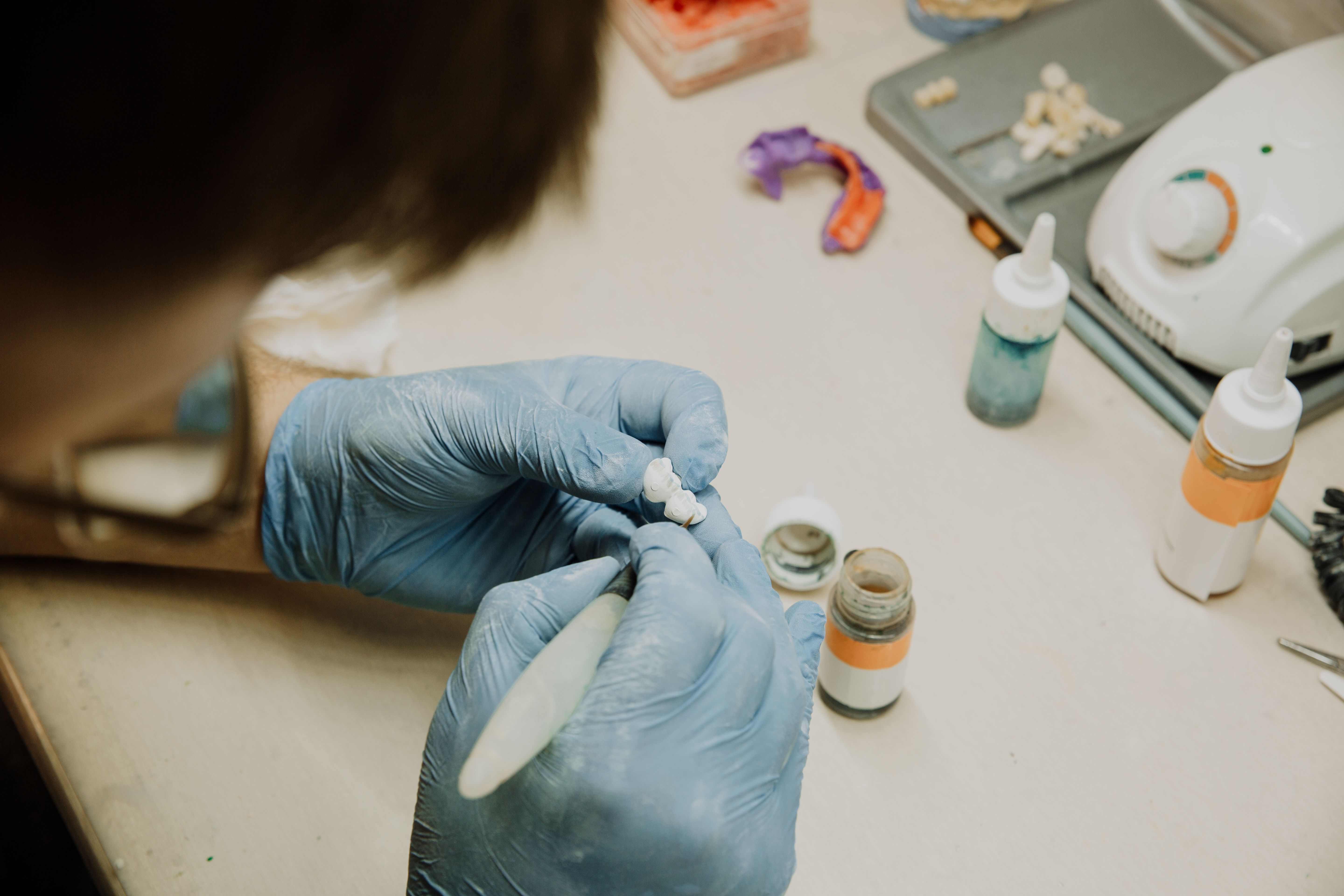 Dental technician shaping a custom restoration at a bench in a dental laboratory