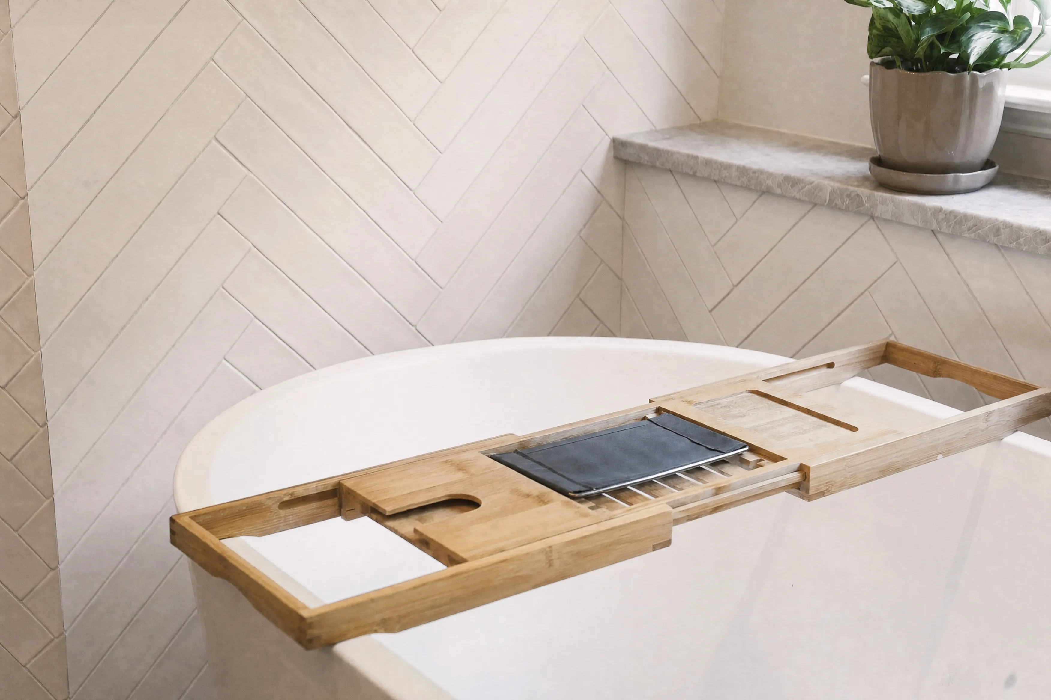 Freestanding tub against a herringbone tile wall with a wooden bath caddy