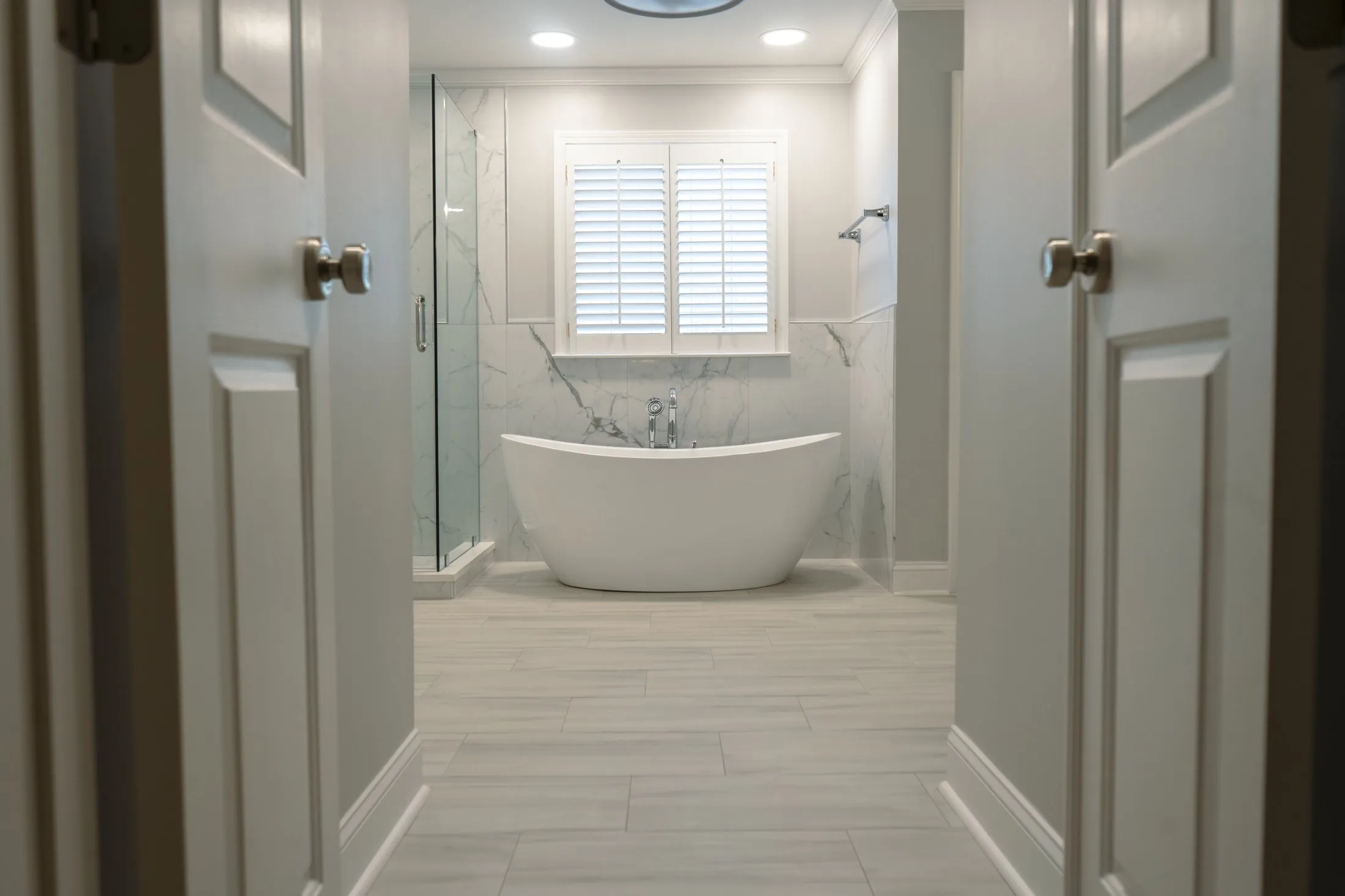 View through double doors into a marble-look master bathroom