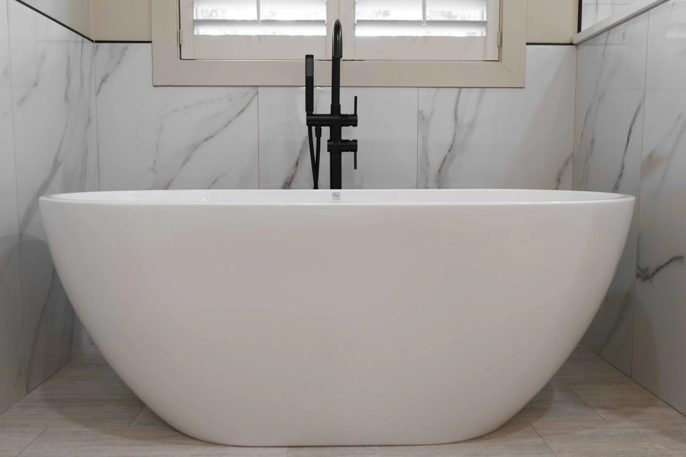 Freestanding tub against a full-height marble-look tile wall