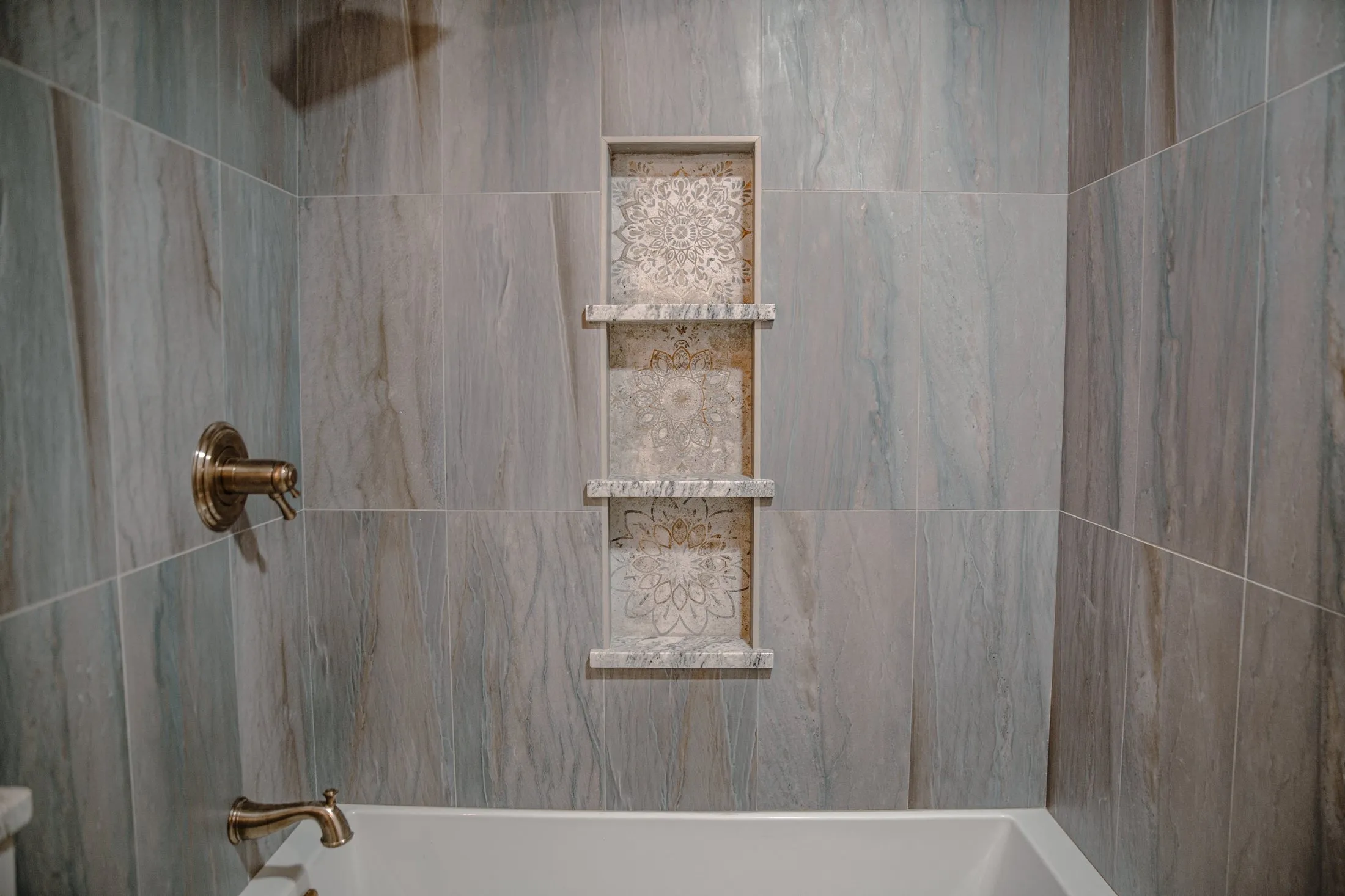 Stone-look tub surround with stacked niches and brass fixtures