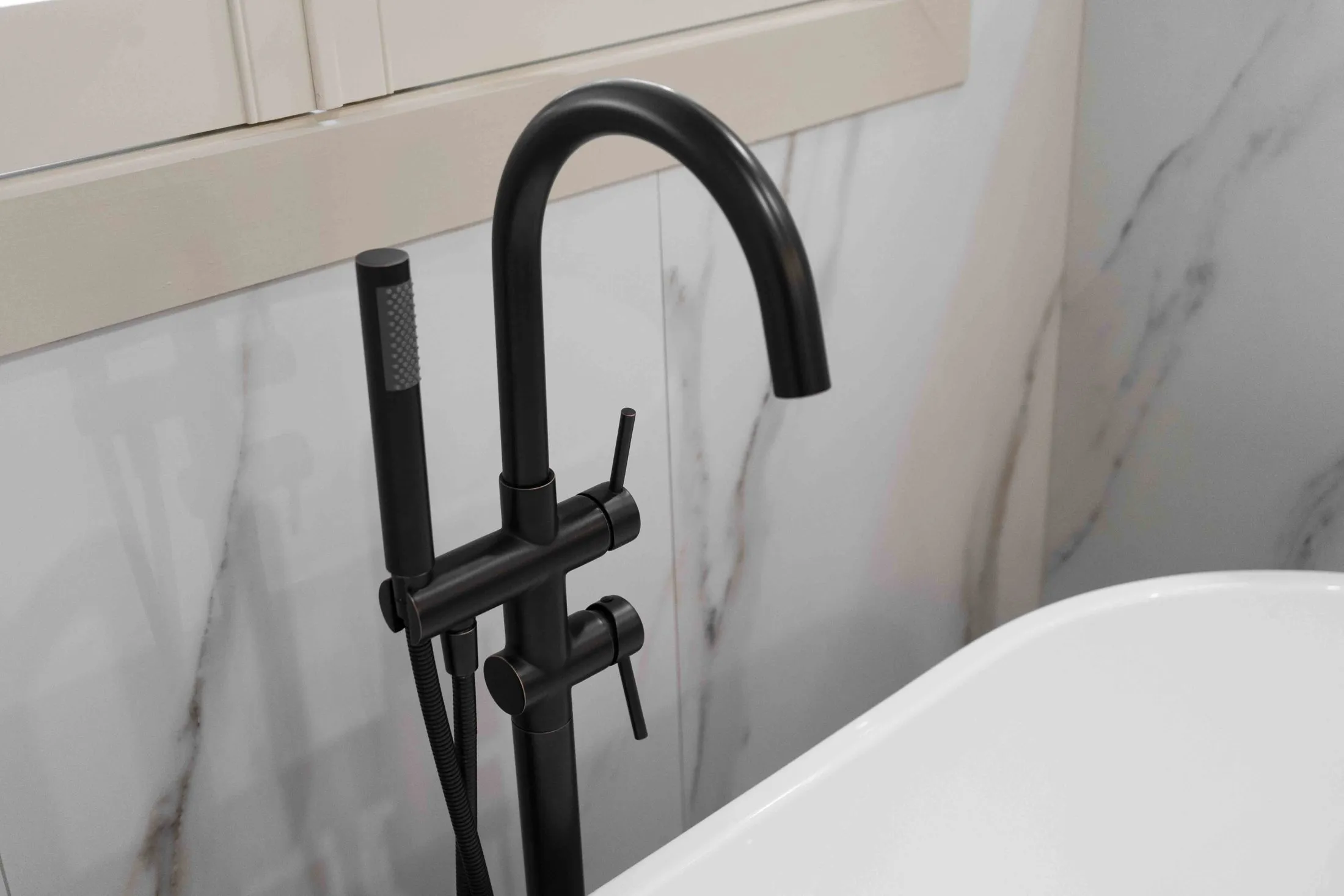 Matte black tub filler against a marble-look tile wall