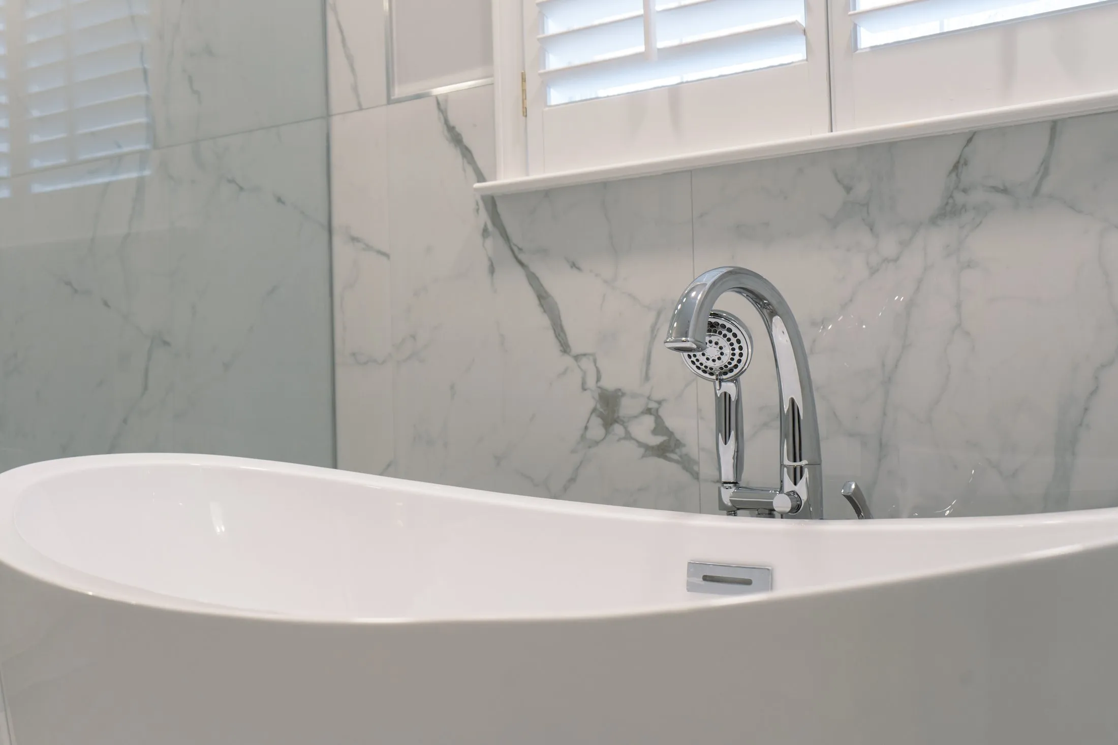Chrome tub filler against a marble-look tile wall