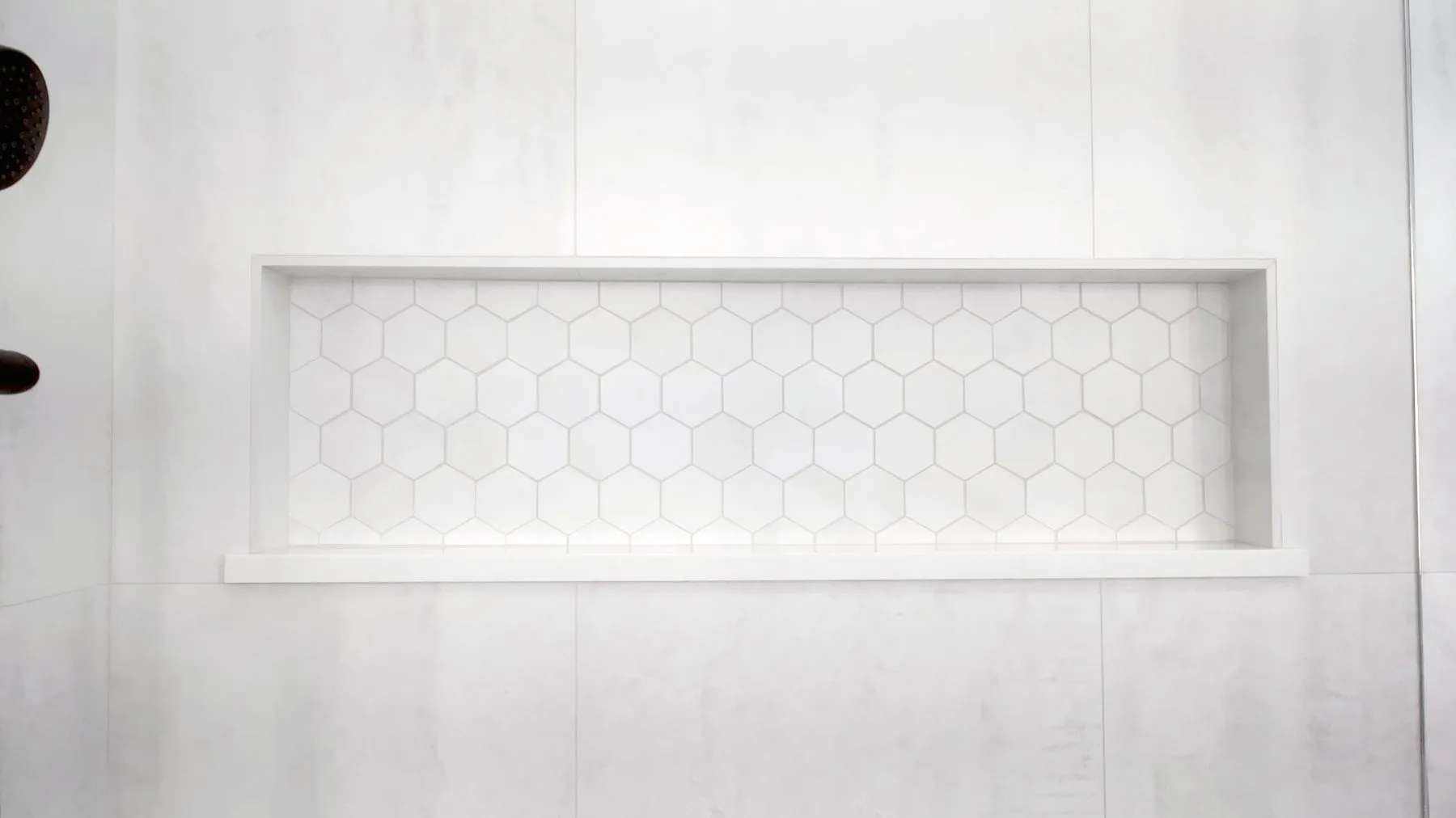 Recessed shower niche lined with white hexagon mosaic tile and a mitred porcelain surround