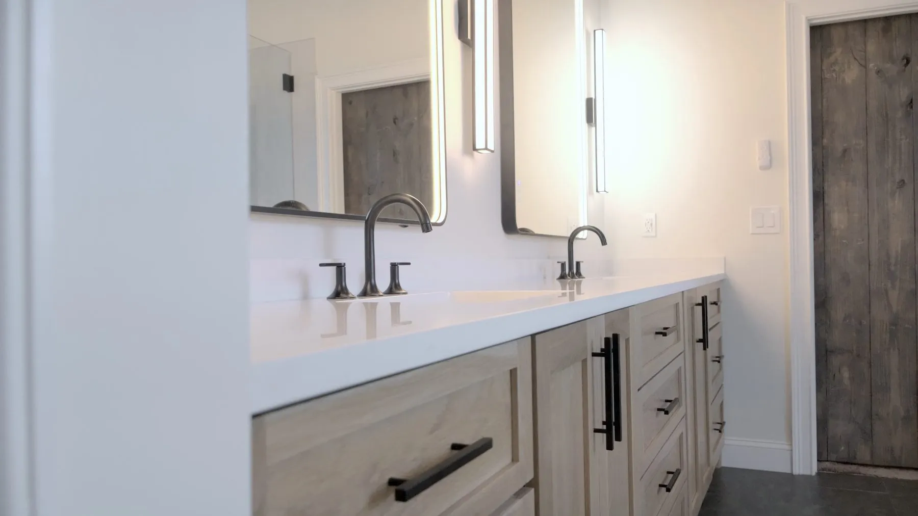 Double vanity with white oak cabinetry, quartz countertop and backlit mirrors in a Peachtree City master bathroom