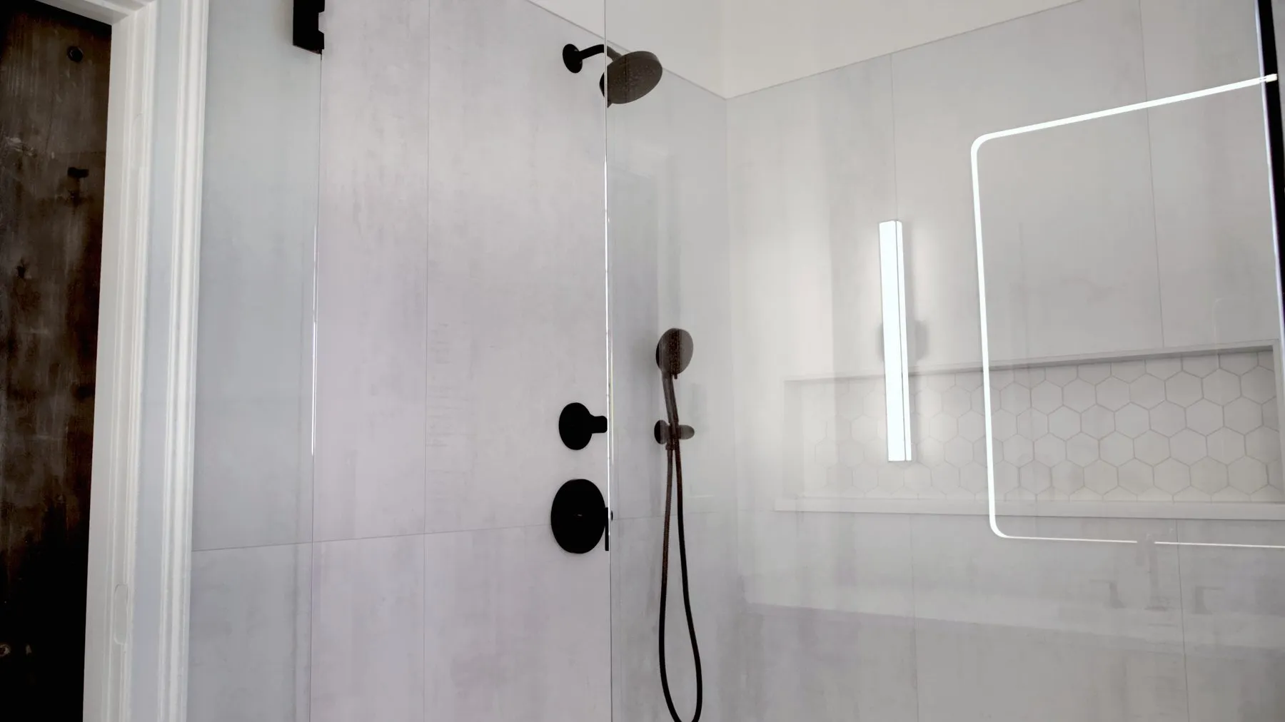 Frameless glass walk-in shower with a hexagon mosaic niche and a backlit mirror
