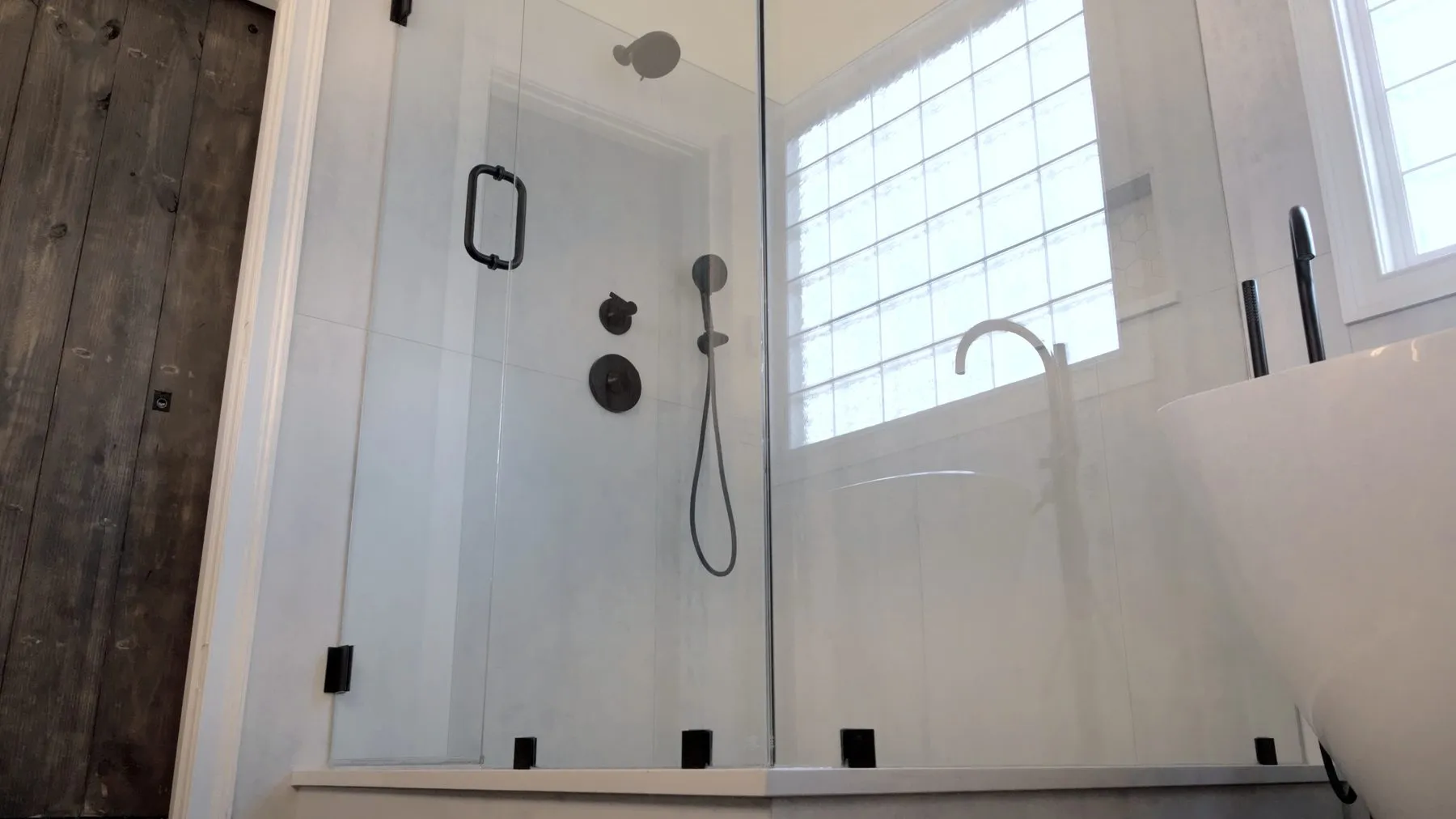 Frameless glass shower enclosure beside a freestanding tub, with a glass block window