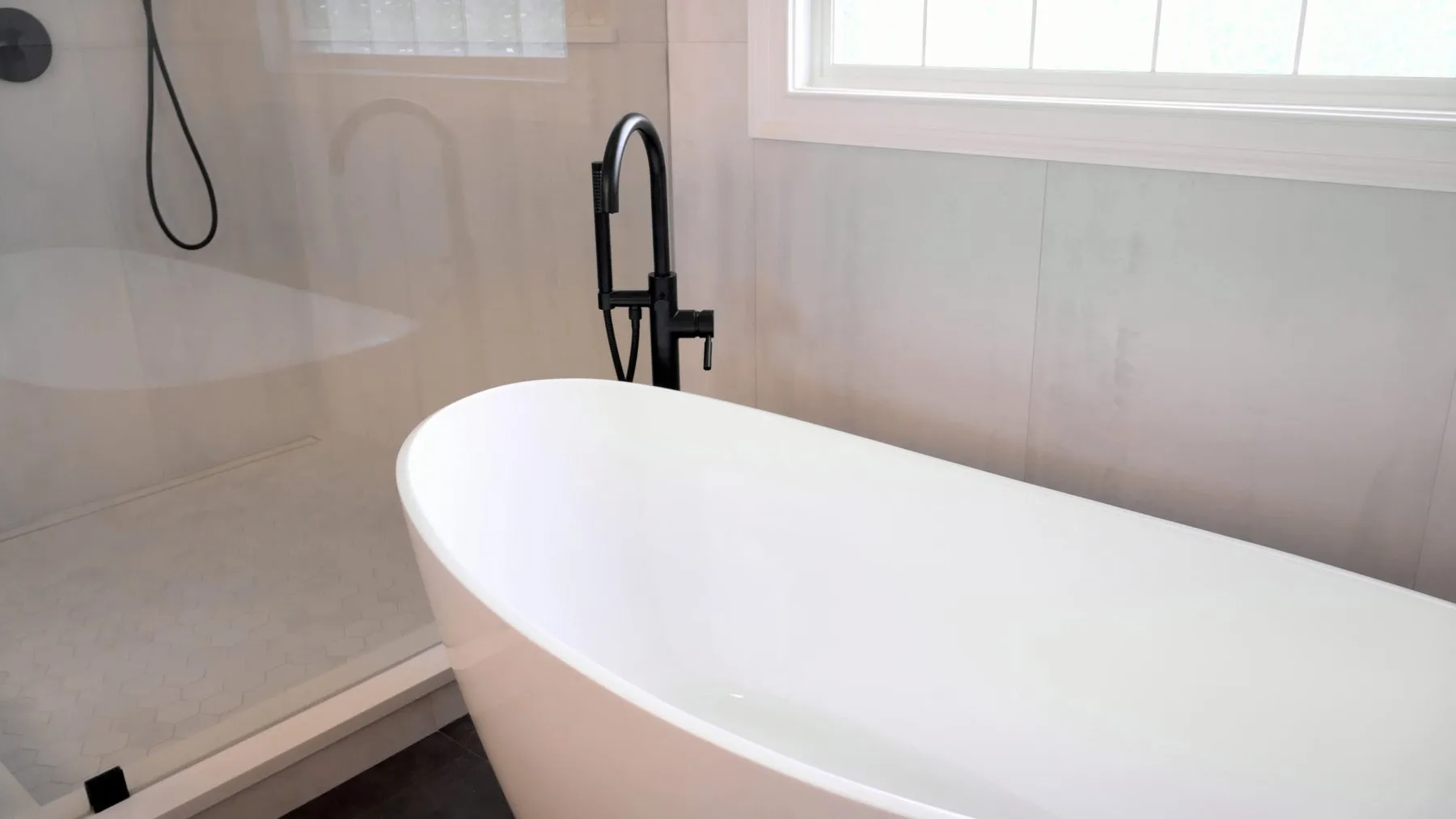 Curbless shower pan in hexagon mosaic tile next to a freestanding soaking tub